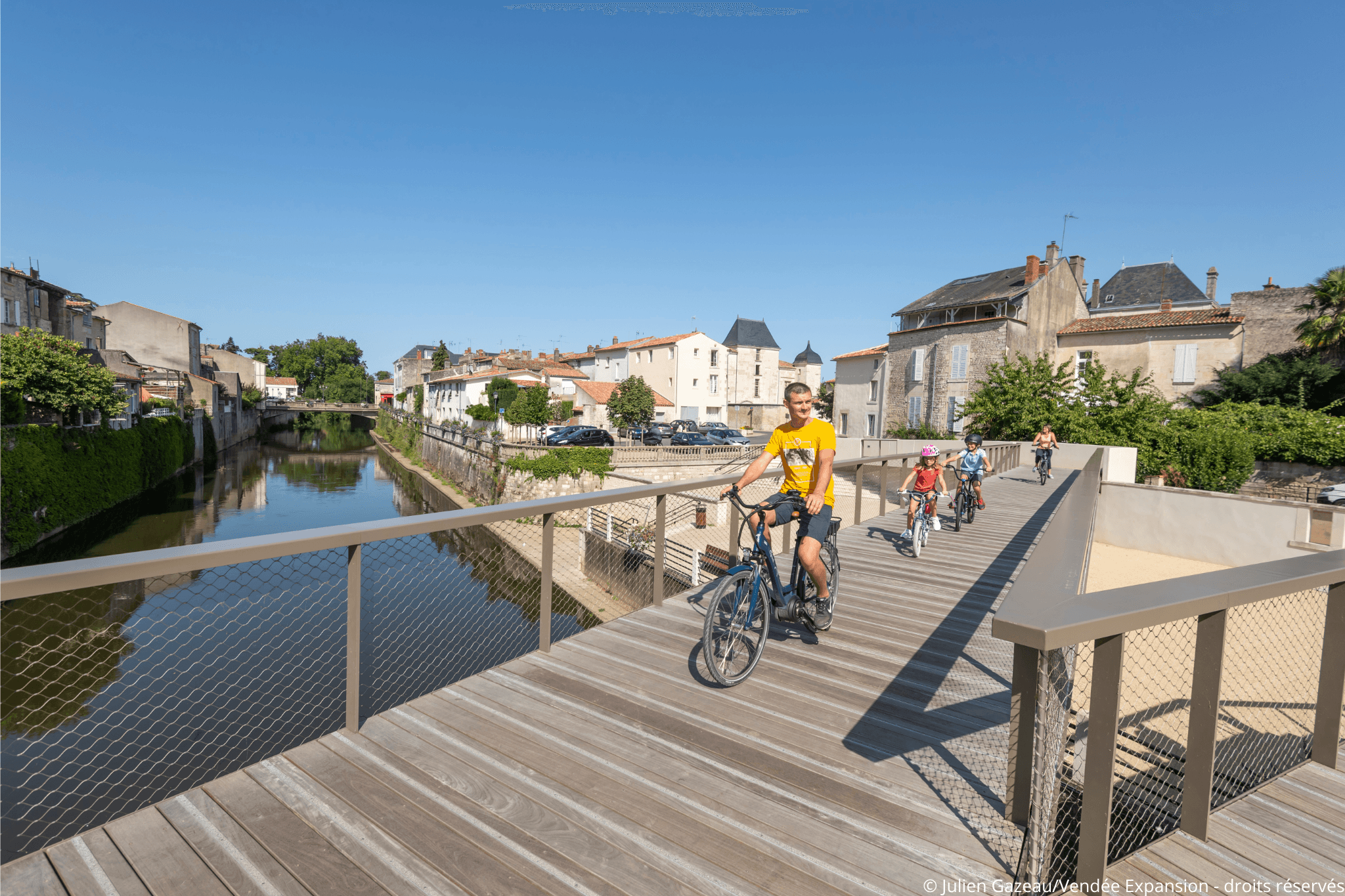 Une famille qui traverse un pont à vélo au dessus la rivière de la Vendée