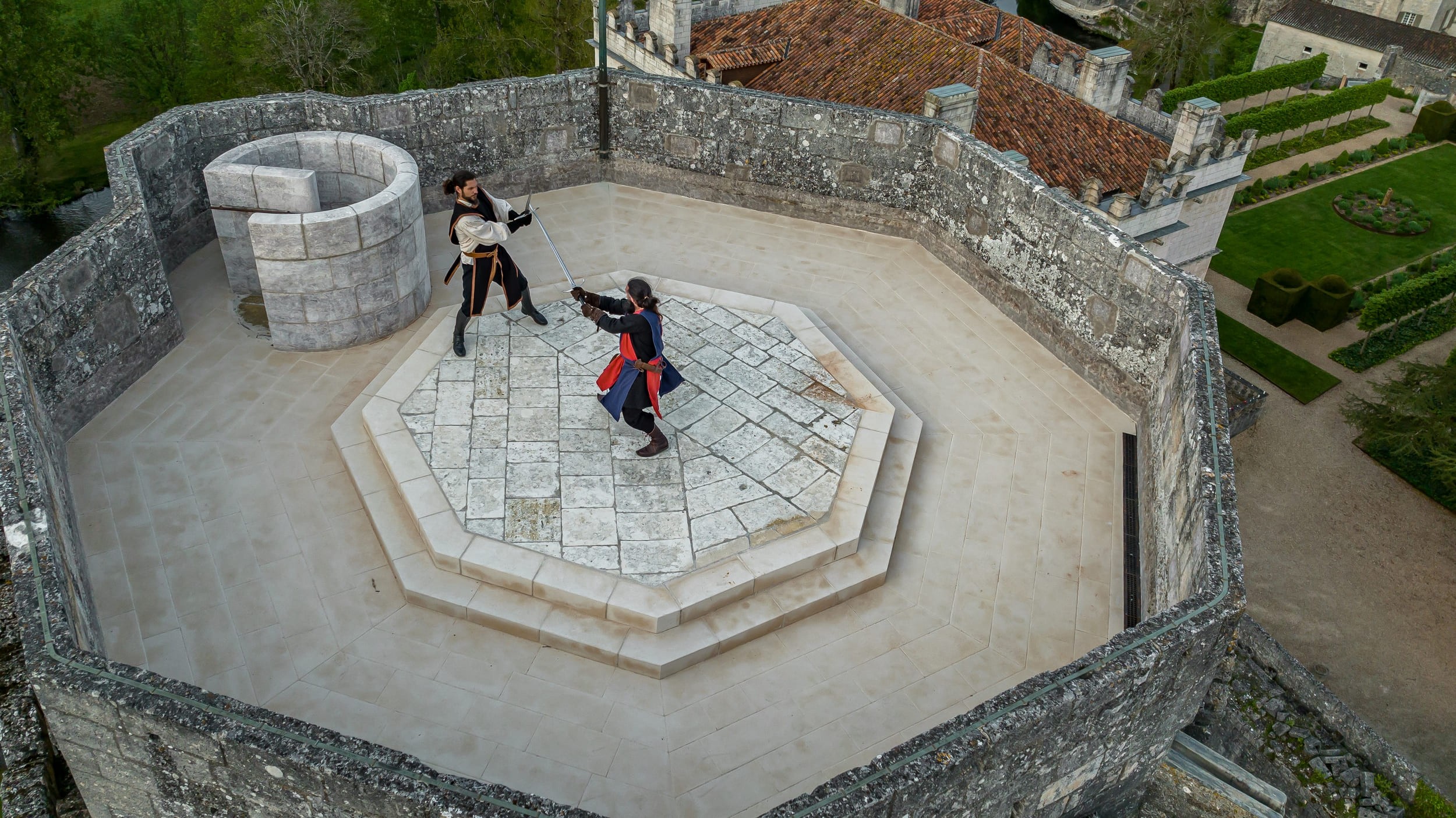 Deux hommes en tenue de chevaliers s'affrontent en duel d'épée sur la tour d'un château.