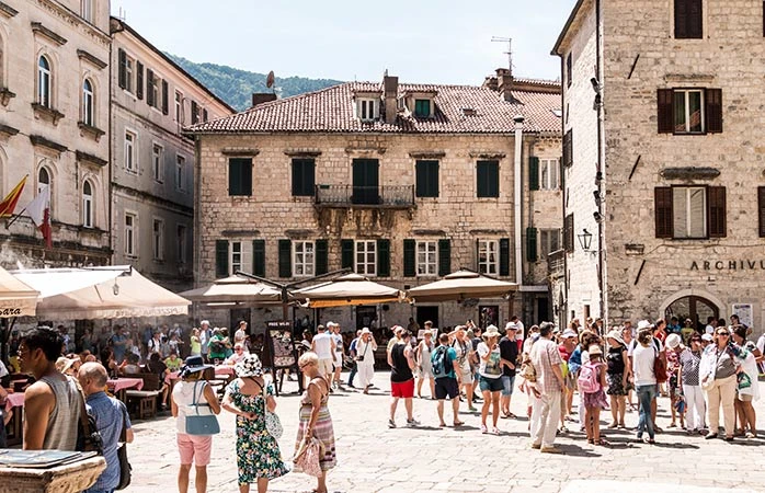 Place animée avec des touristes en terrasse et des bâtiments historiques autour, sous un ciel ensoleillé.