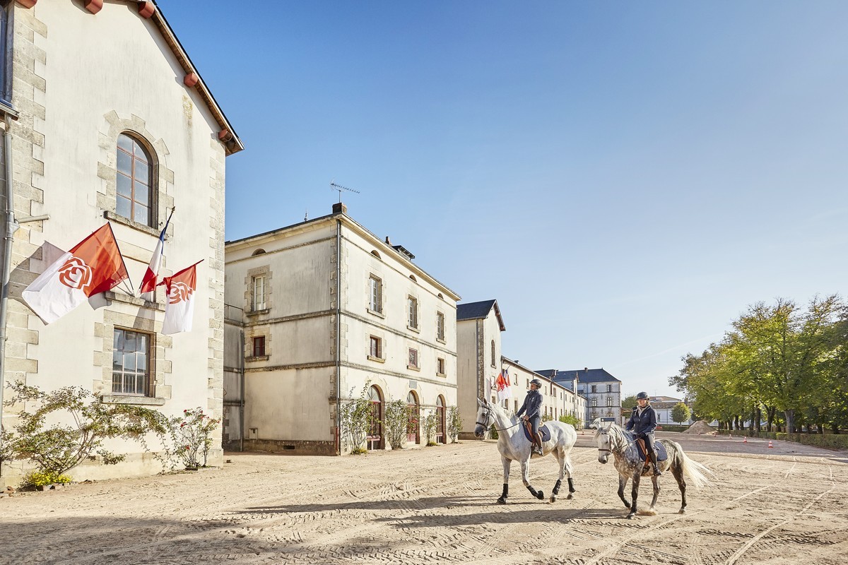 Deux chevaux avec leur cavalier dans la cours du Haras de la Vendée devant un bâtiment historique