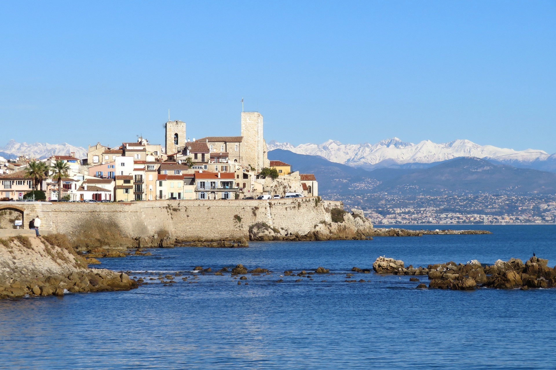 Point de vue emblématique sur le centre historique d’Antibes au premier plan et sur le Mercantour enneigé en toile de fond sous un ciel bleu