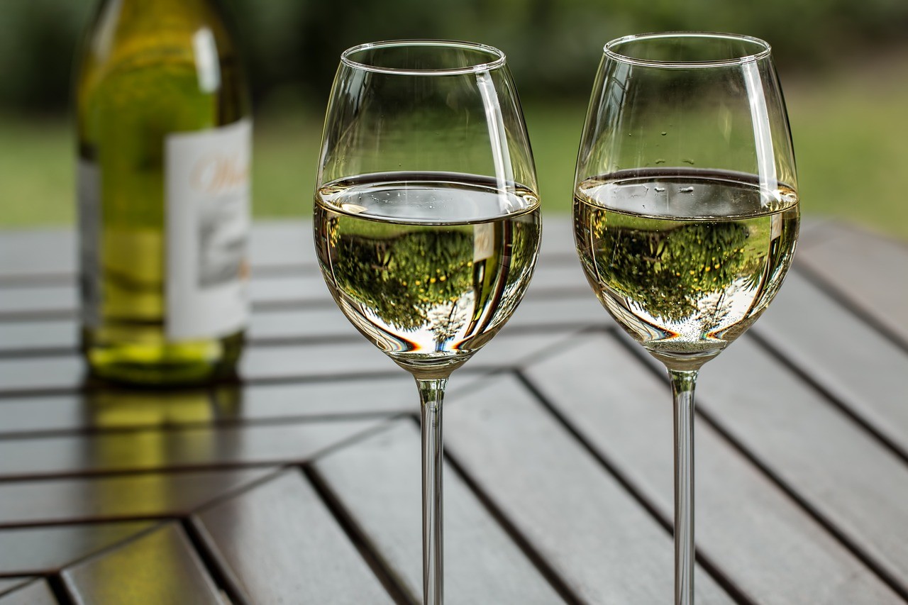 Deux verres de vin blanc sur une table extérieure en bois avec une bouteille en arrière-plan
