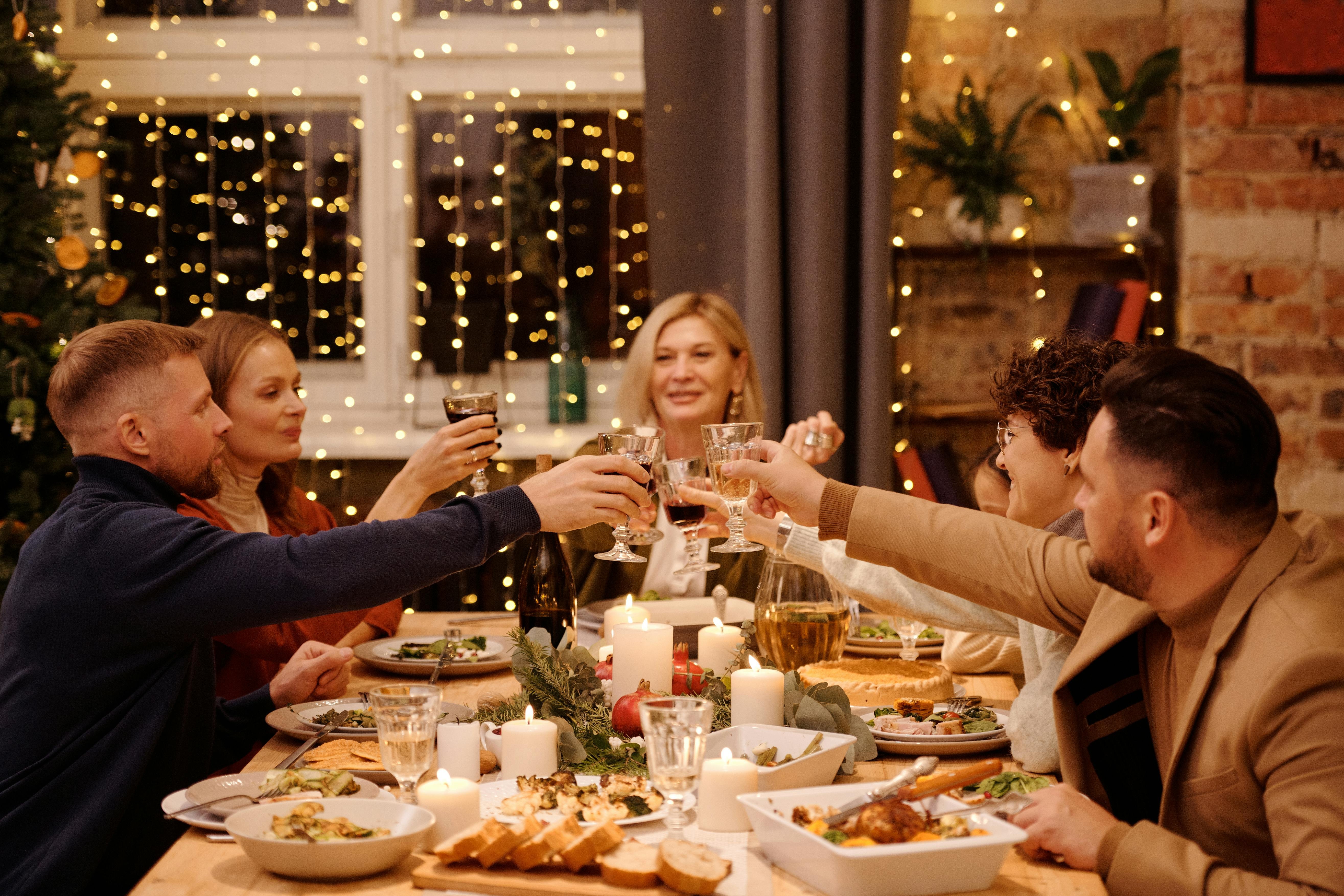 Groupe d'amis partageant un dîner festif avec des lumières scintillantes en arrière-plan.