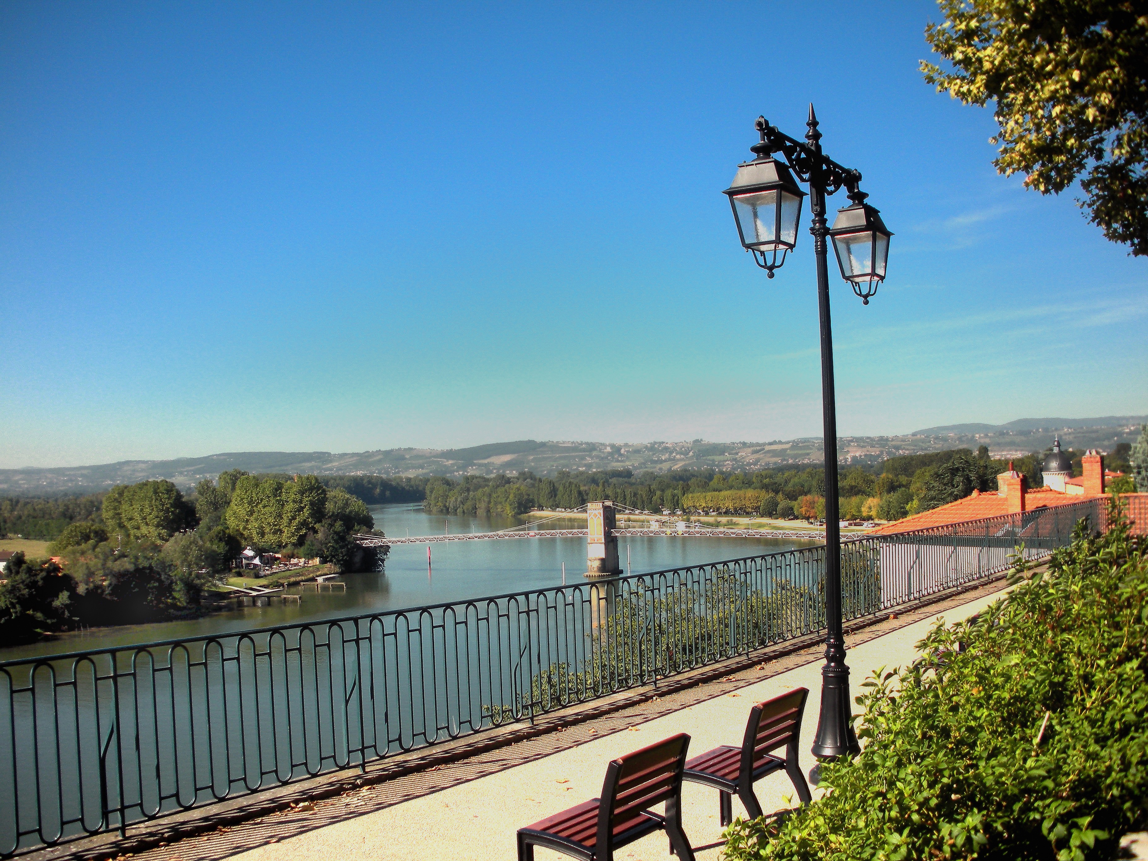 Vue sur la Saône avec la passerelle depuis Trévoux avec en arrière plan les villages montagneux sous un ciel bleu.