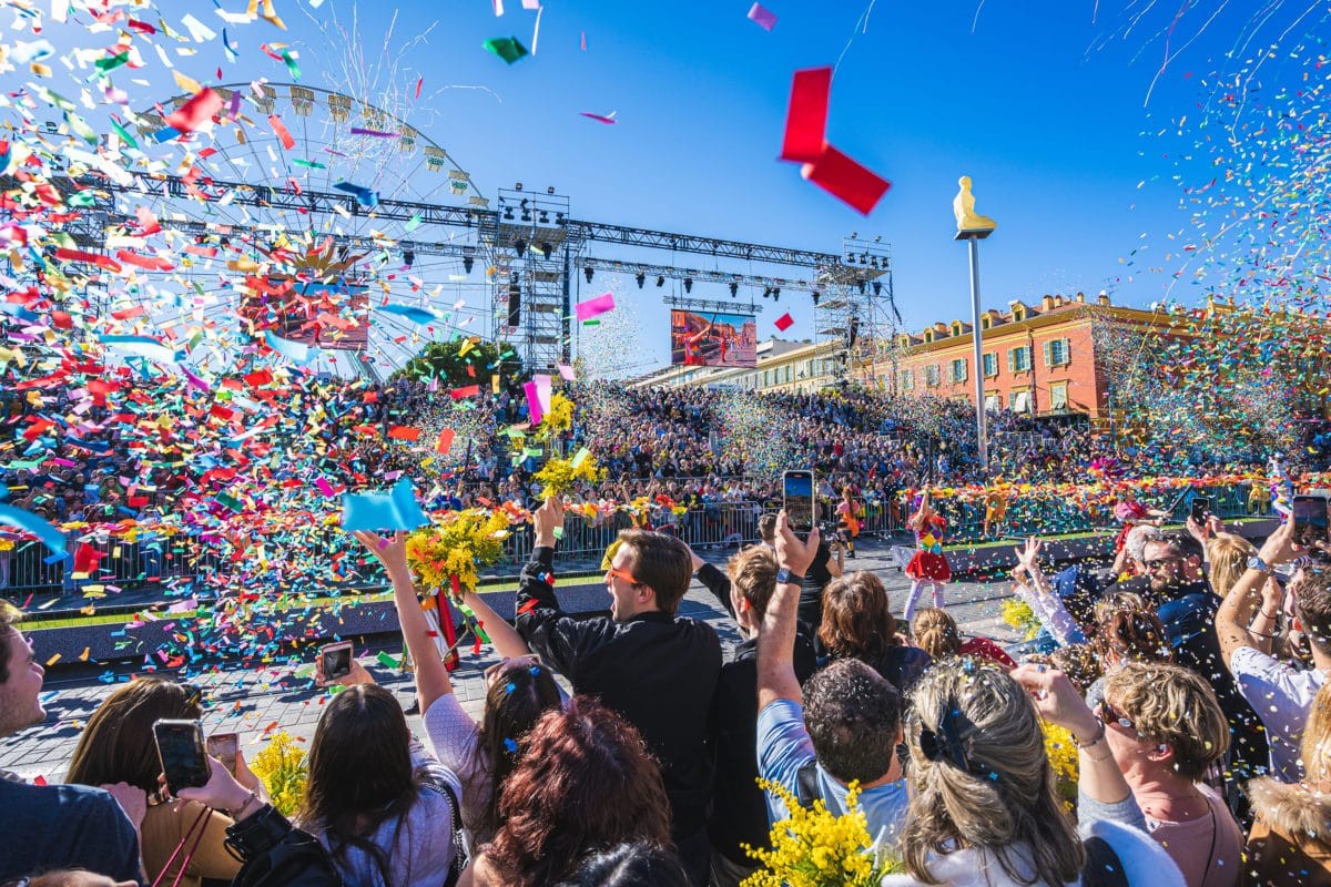 Scène festive et colorée du Carnaval de Nice avec confettis et foule enthousiaste.