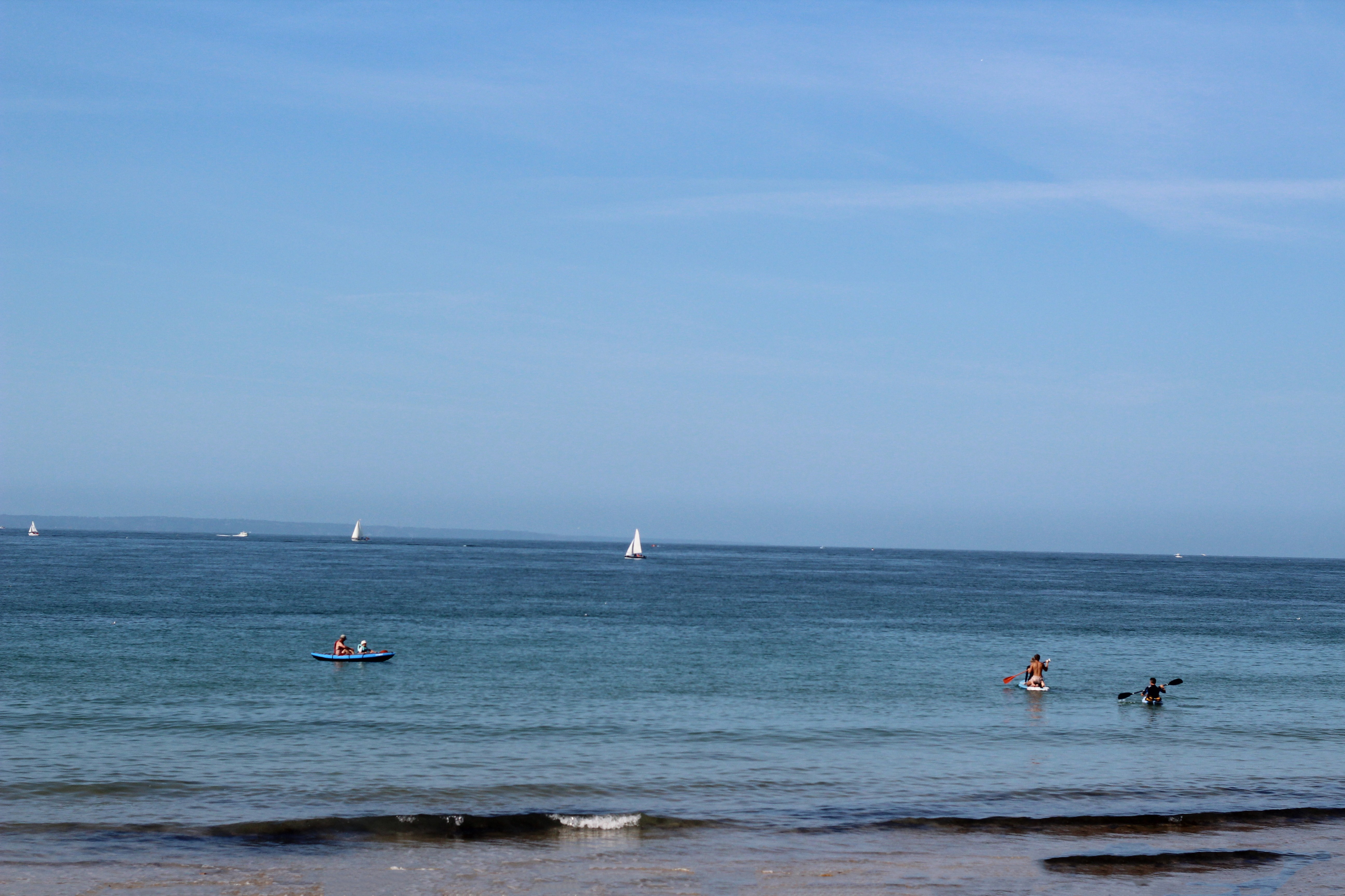Plan sur la mer calme de diffrent tons de bleus, des bateaux vont vers l'ile de Jersey, touristes faisant du paddle ou du kayak . Journée ensoleillée.