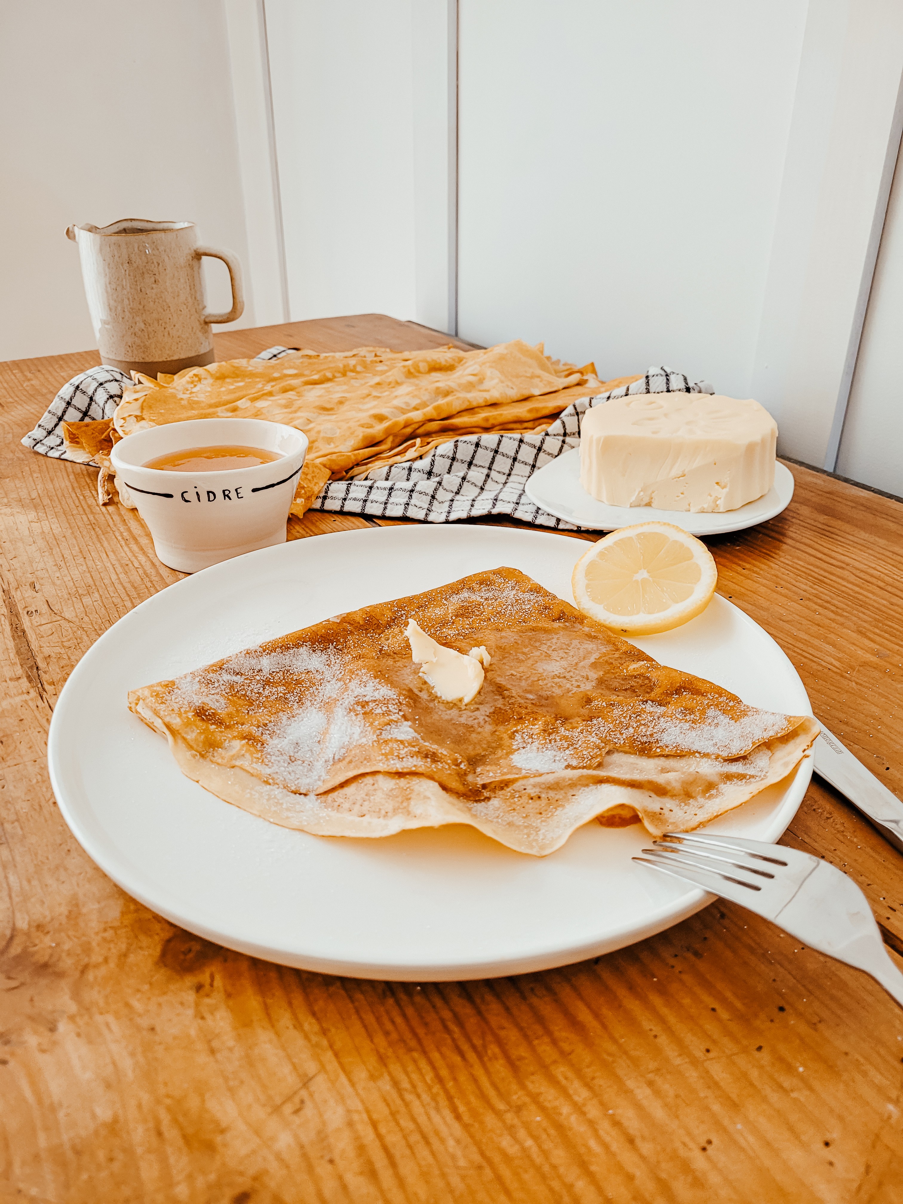 Crêpes avec du sucre et du beurre et une bolée de cidre sur une table