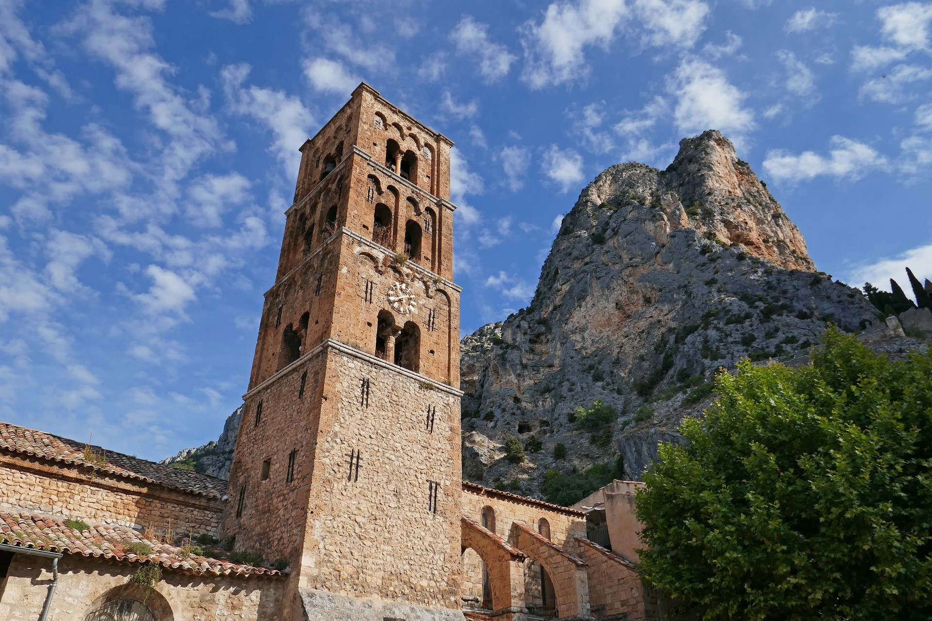Les falaises adossées au village de Moustiers-Sainte-Marie vues depuis le pied de son église, avec un ciel bleu tacheté de nuages 