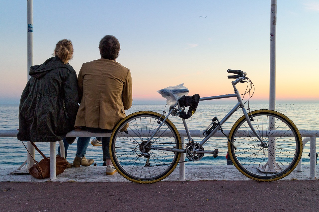 Un couple assis sur un banc au bord de la mer avec un vélo, au coucher du soleil.