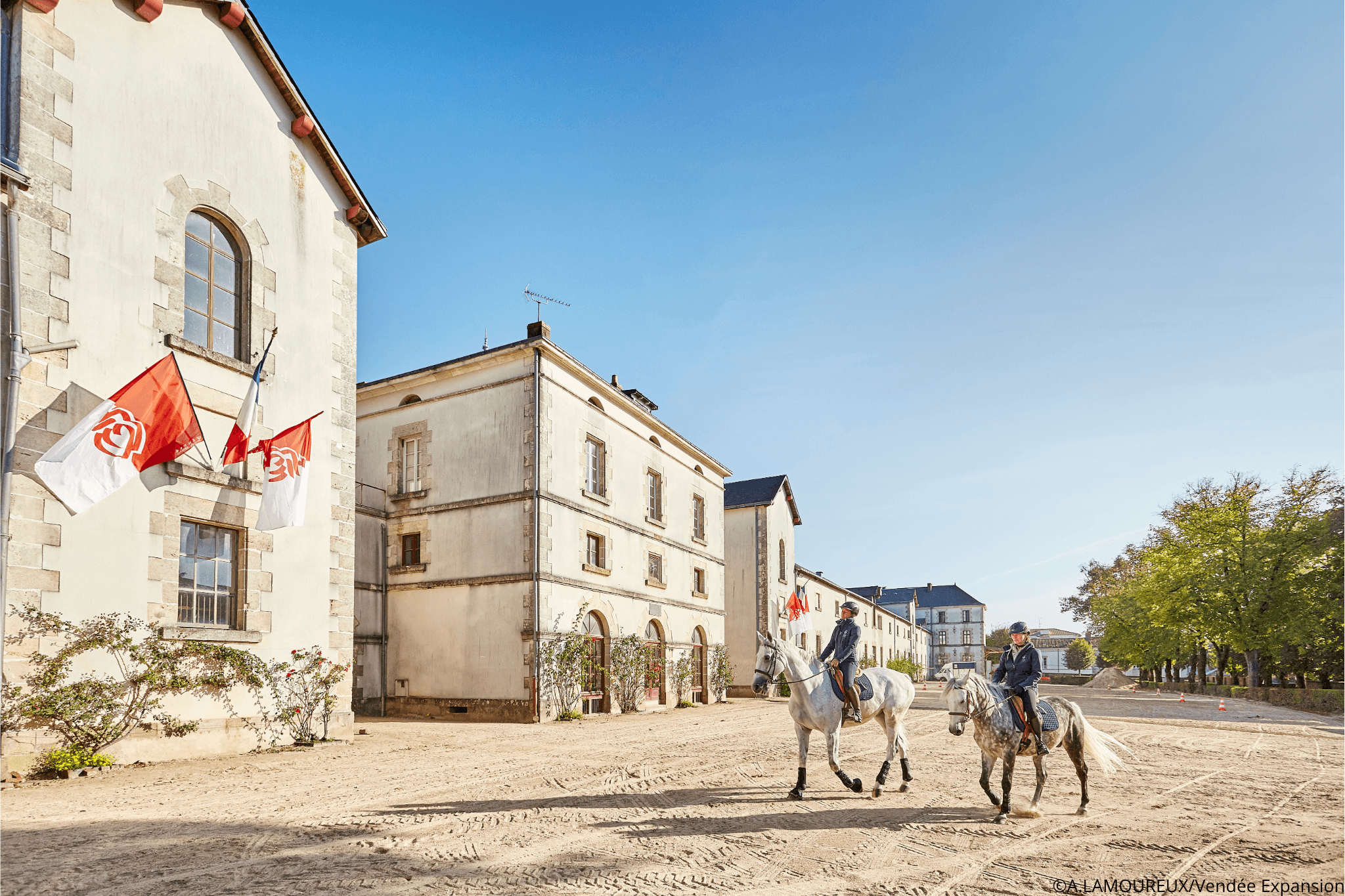 Deux chevaux avec leur cavalier dans la cours du Haras de la Vendée devant un bâtiment historique