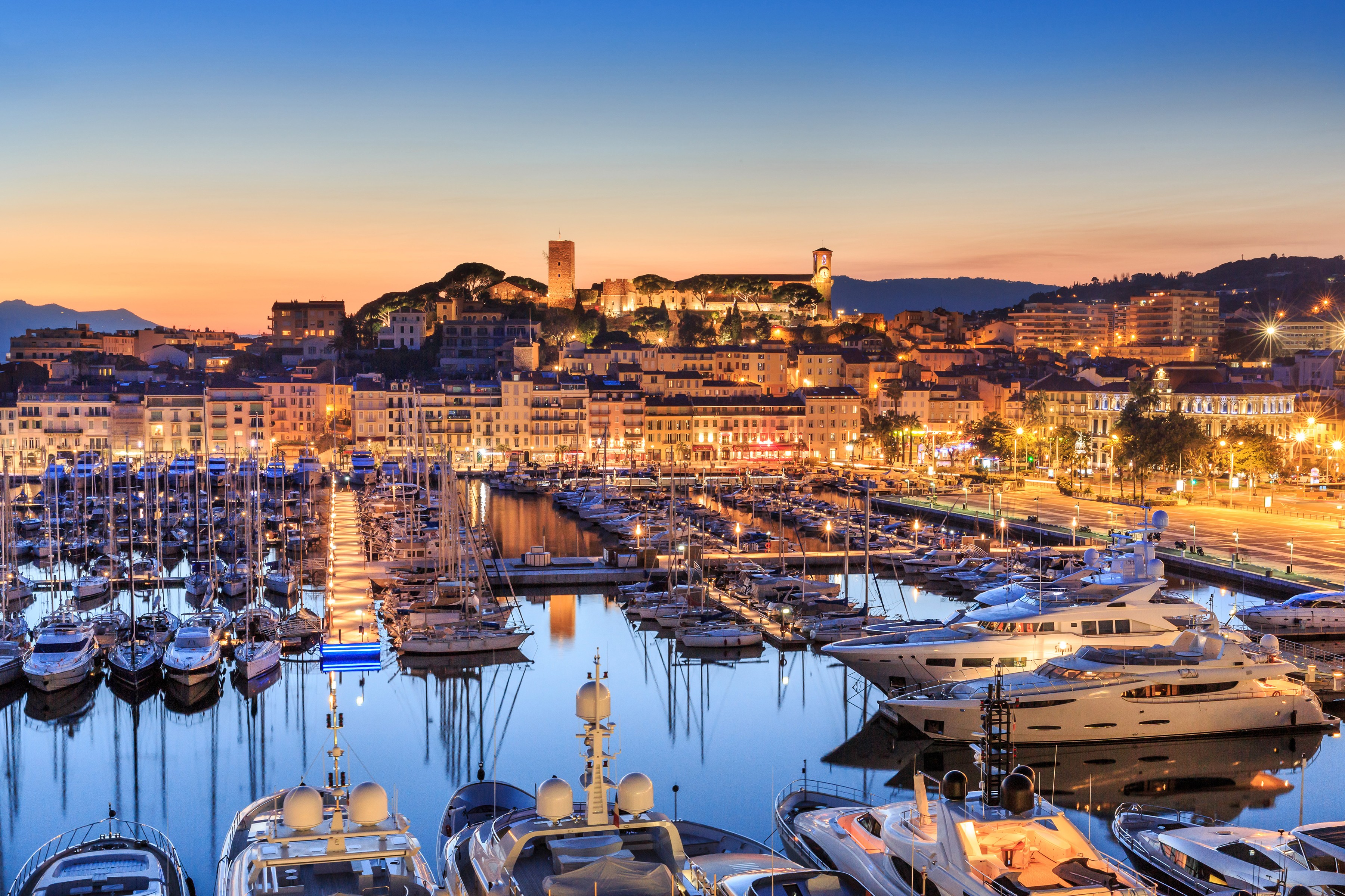 Vue aérienne du port de Cannes et du quartier historique du Suquet illuminés par les lumières de la ville au début de la nuit