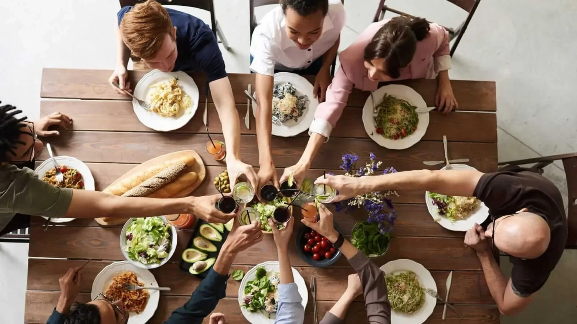 Groupe d'amis partageant un repas et trinquant autour d'une table en bois avec des plats variés.