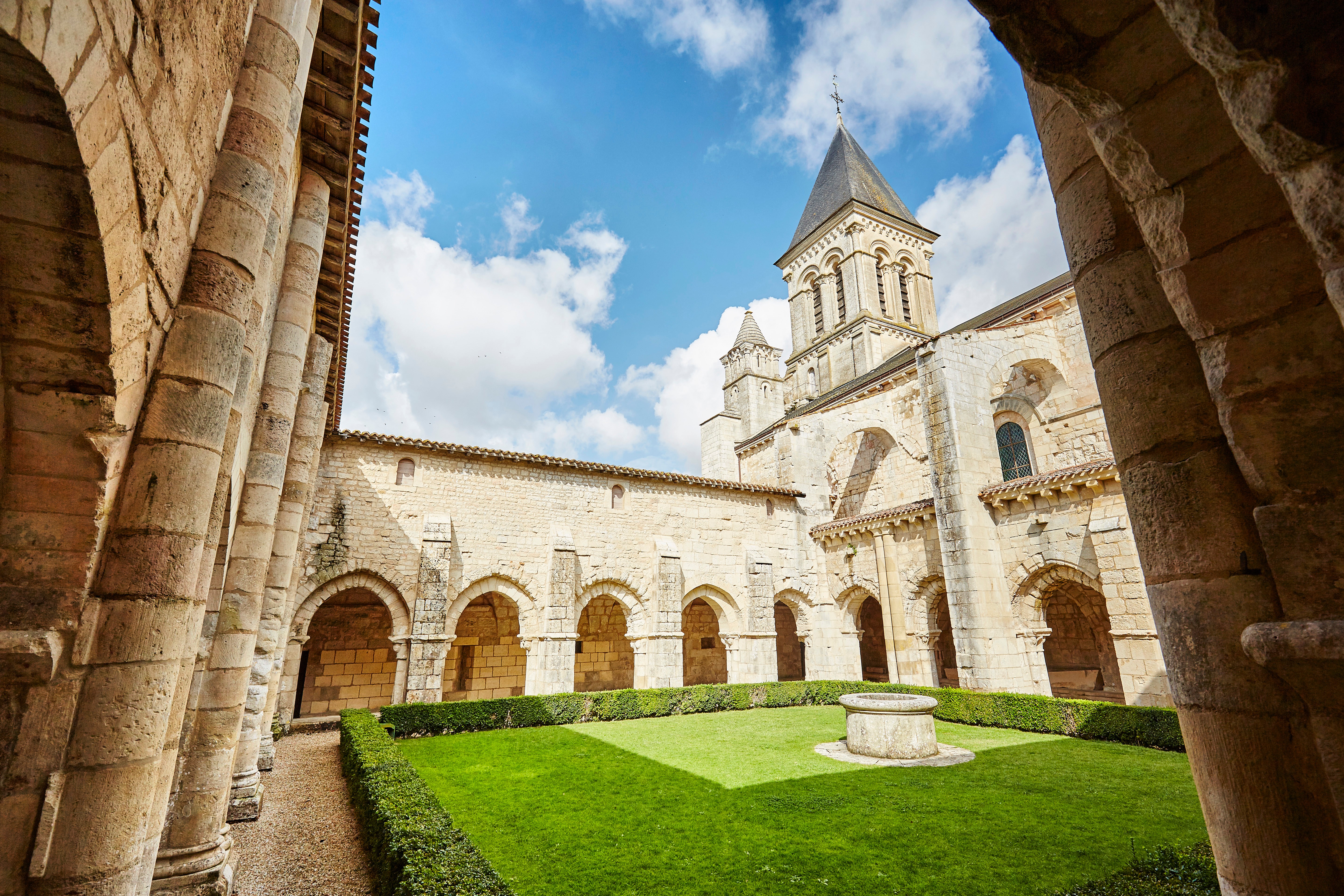 Cloître de l’Abbaye avec voûtes en arc autour du jardin d’herbe et de haies carré du monastère et au second plan, le clocher de l’abbatiale