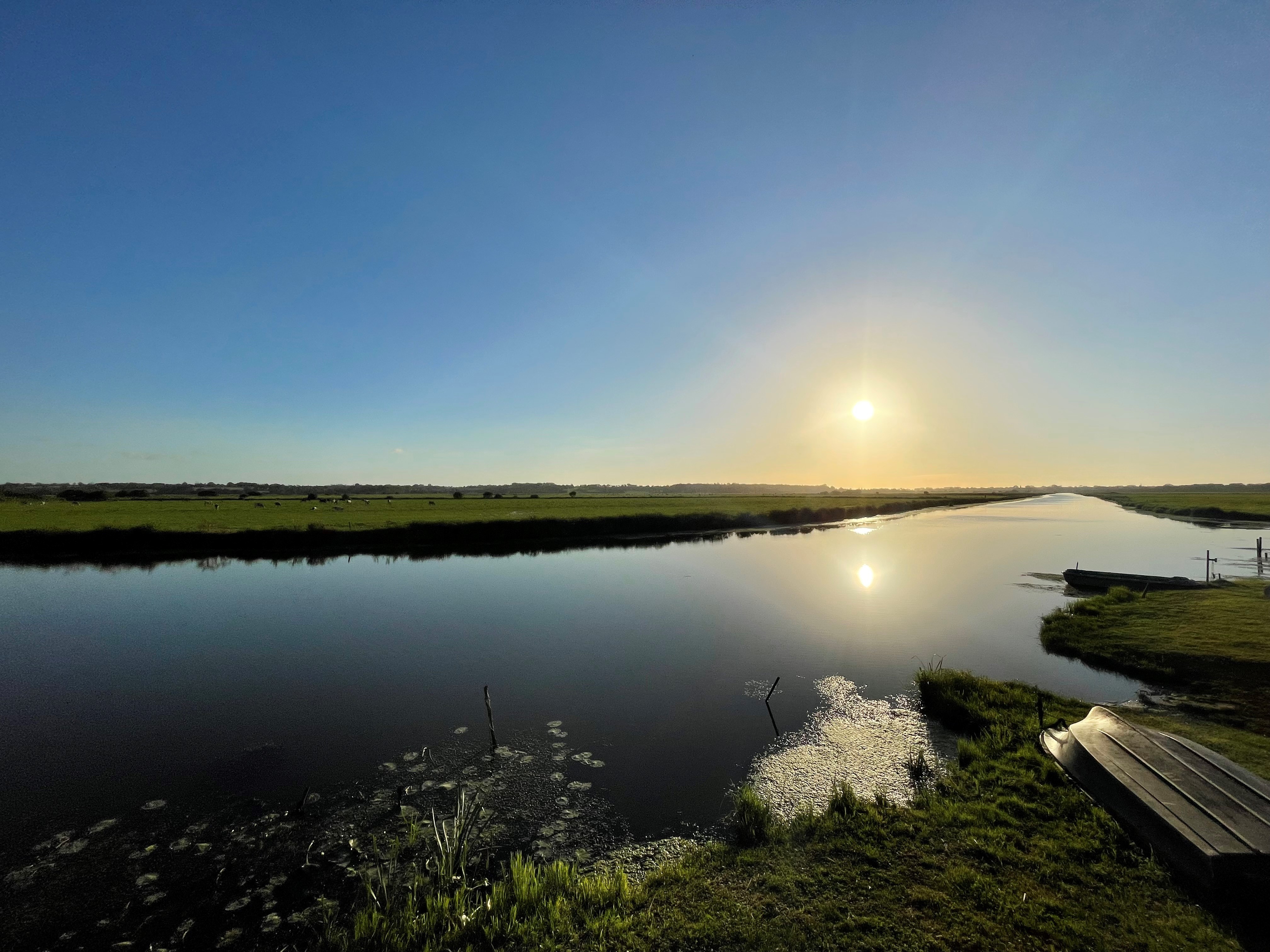 Coucher de soleil sur la rivière Douve dans les marais du Cotentin, soleil  bas dans le ciel, projetant une lumière chaude et orangée sur le paysage. paysage naturel paisible