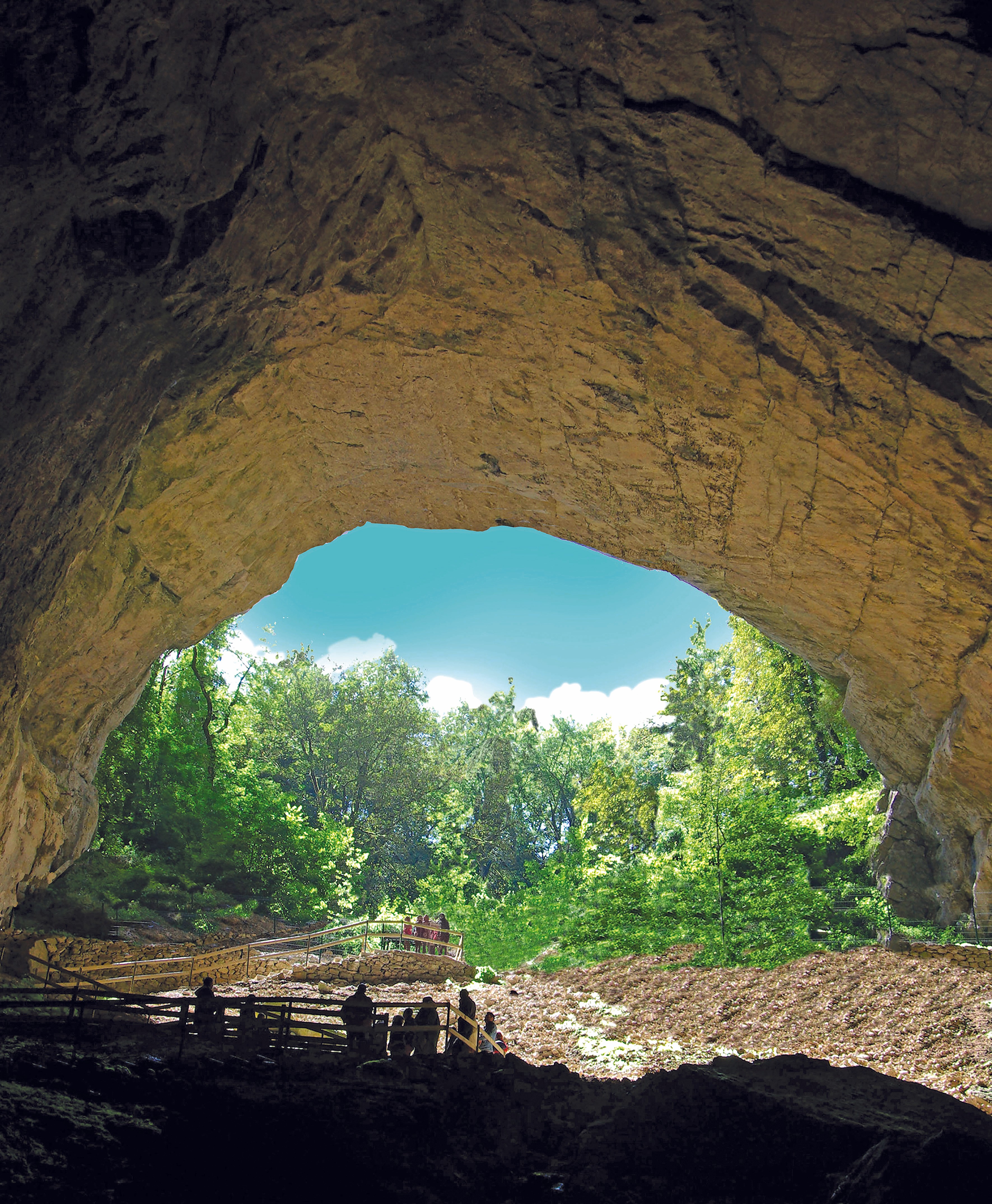Entrée de la grotte de Cerdon sous un ciel bleu et une végétation verdoyantes.