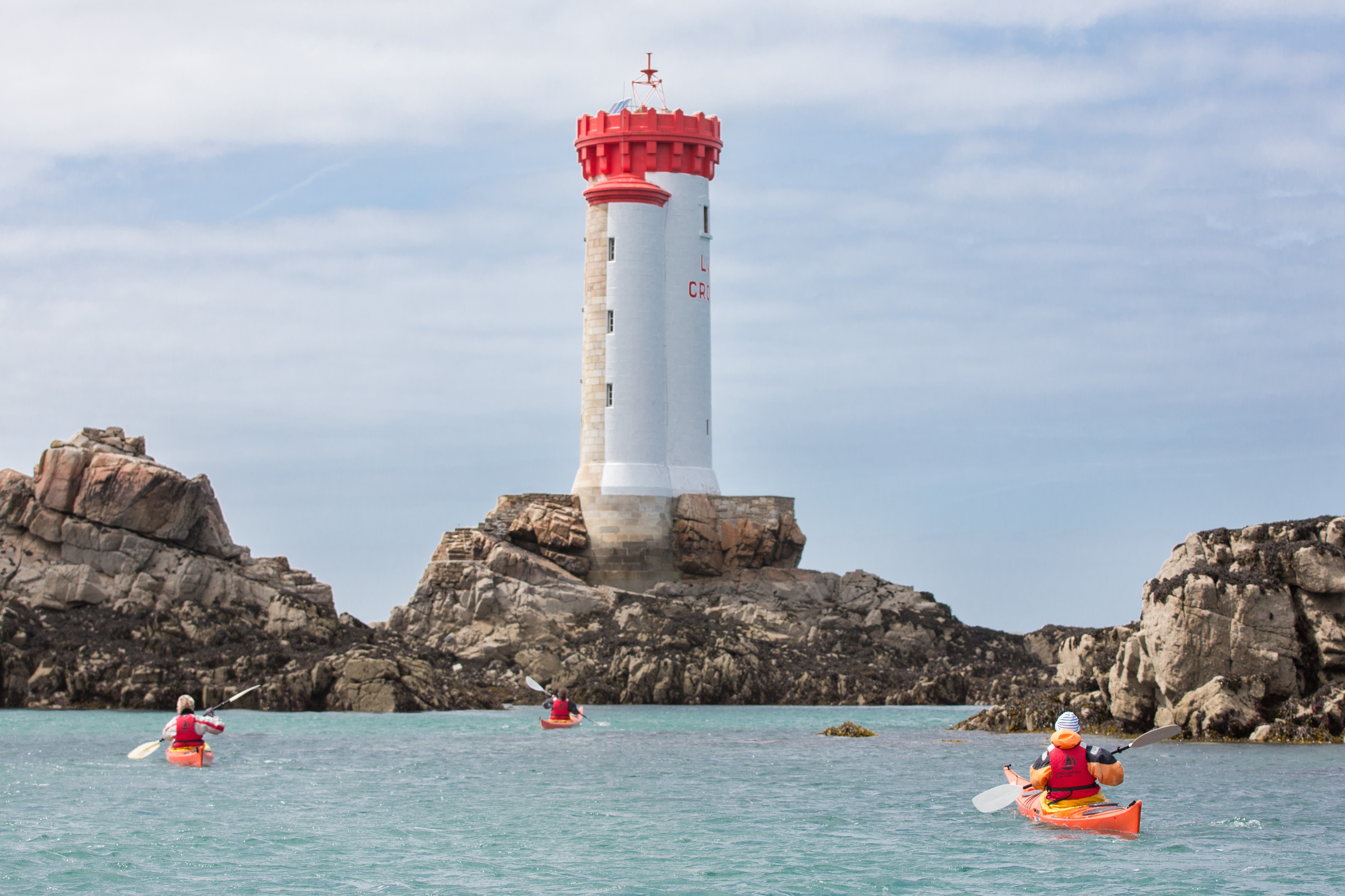 Vue depuis la mer sur le phare du paon sur l’île de Bréhat, couleur blanc et rouge, avec des kayakistes sur l’eau