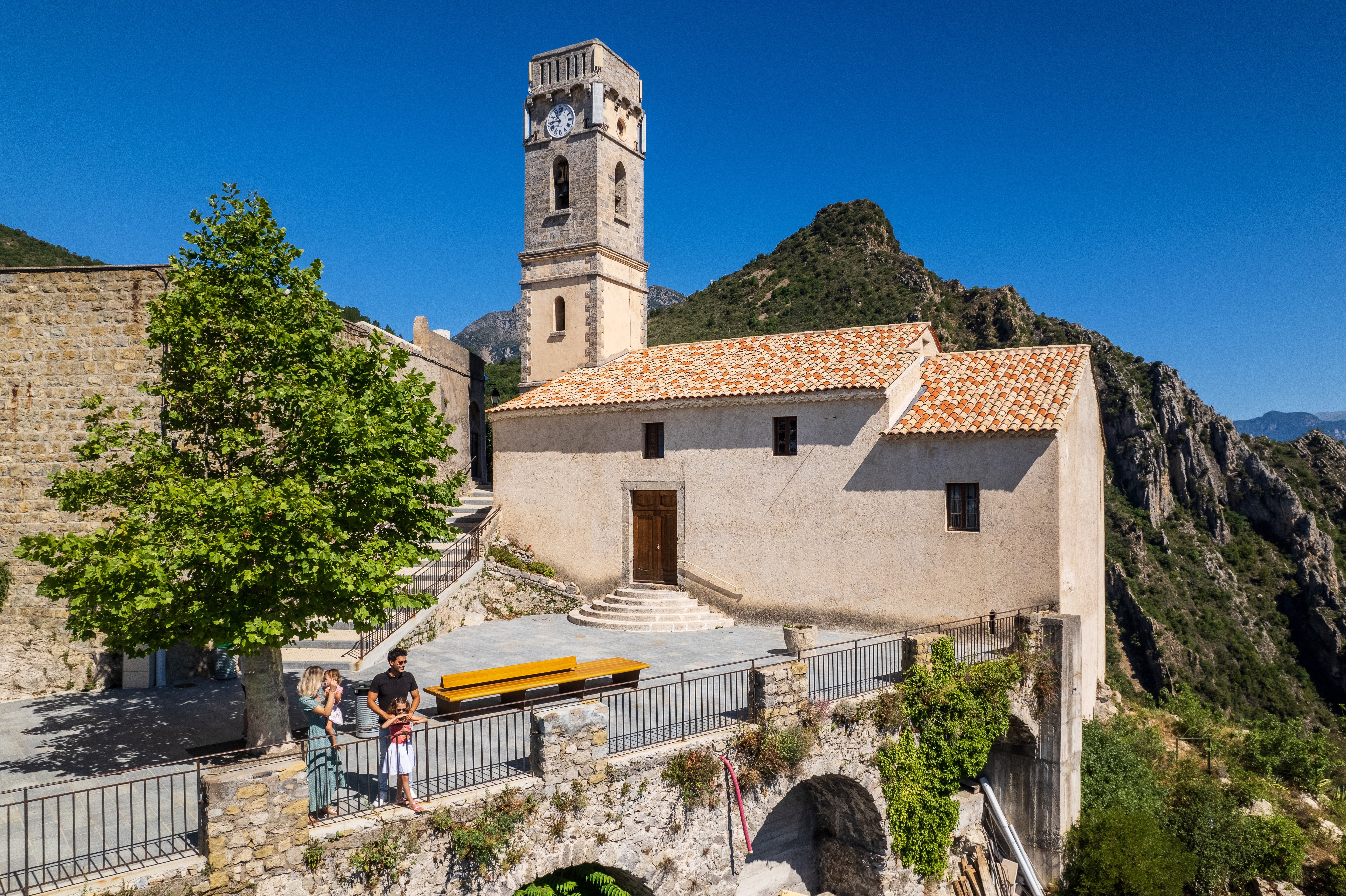 Église du village perché de Bonson sous un ciel bleu vue par un drone avec une famille profitant du paysage au premier plan