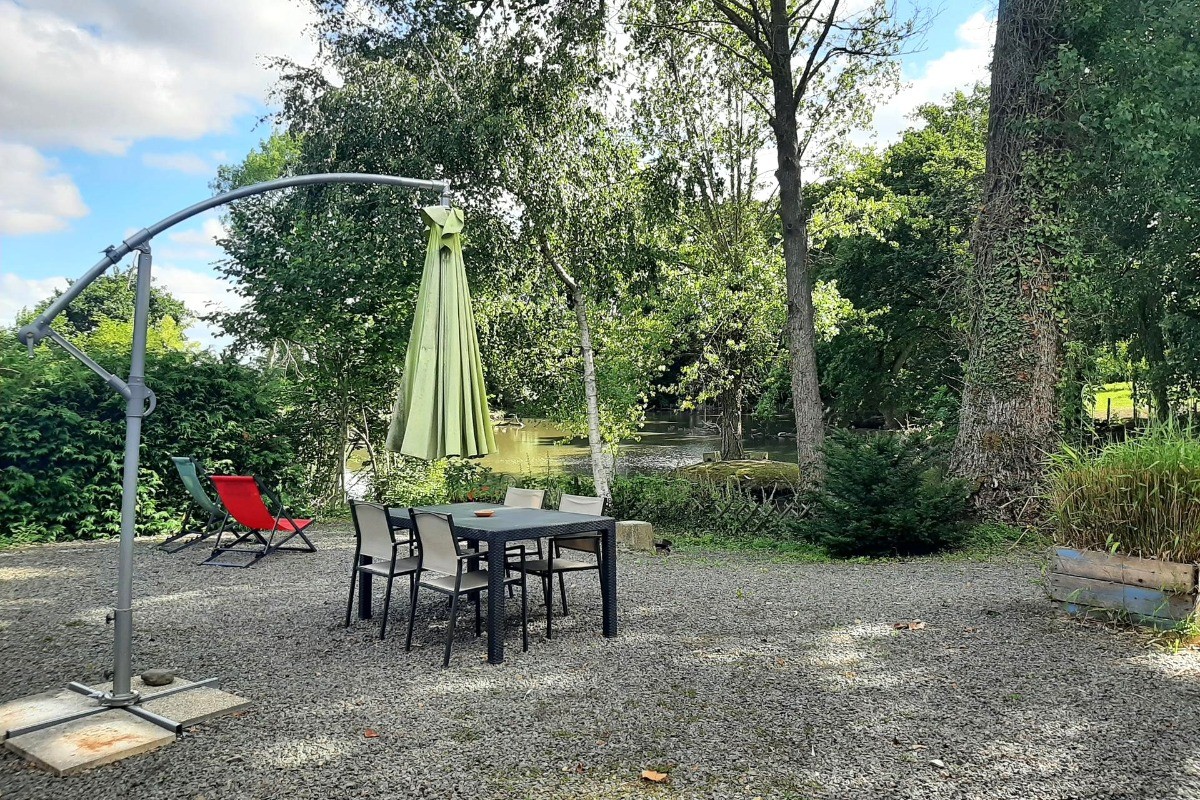 Terrasse privative à la location, son salon de jardin, parasol, transats et vue sur l'étang.