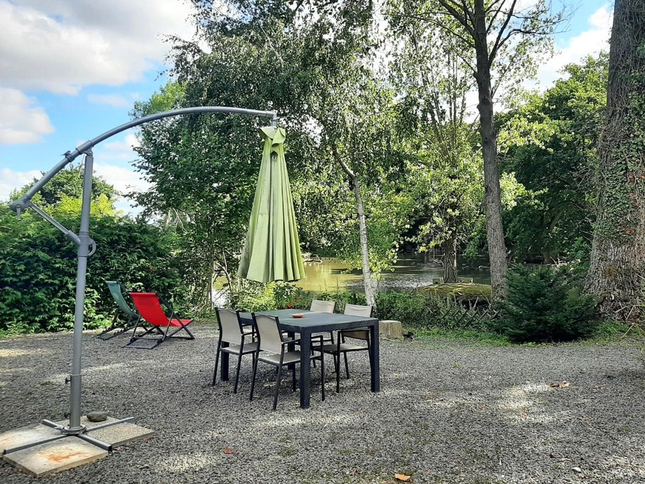 Terrasse privative à la location, son salon de jardin, parasol, transats et vue sur l'étang.