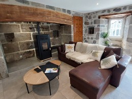 Salon chaleureux du gîte La Petite Maison avec poêle à granulés, canapé d'angle et murs en pierres apparentes.