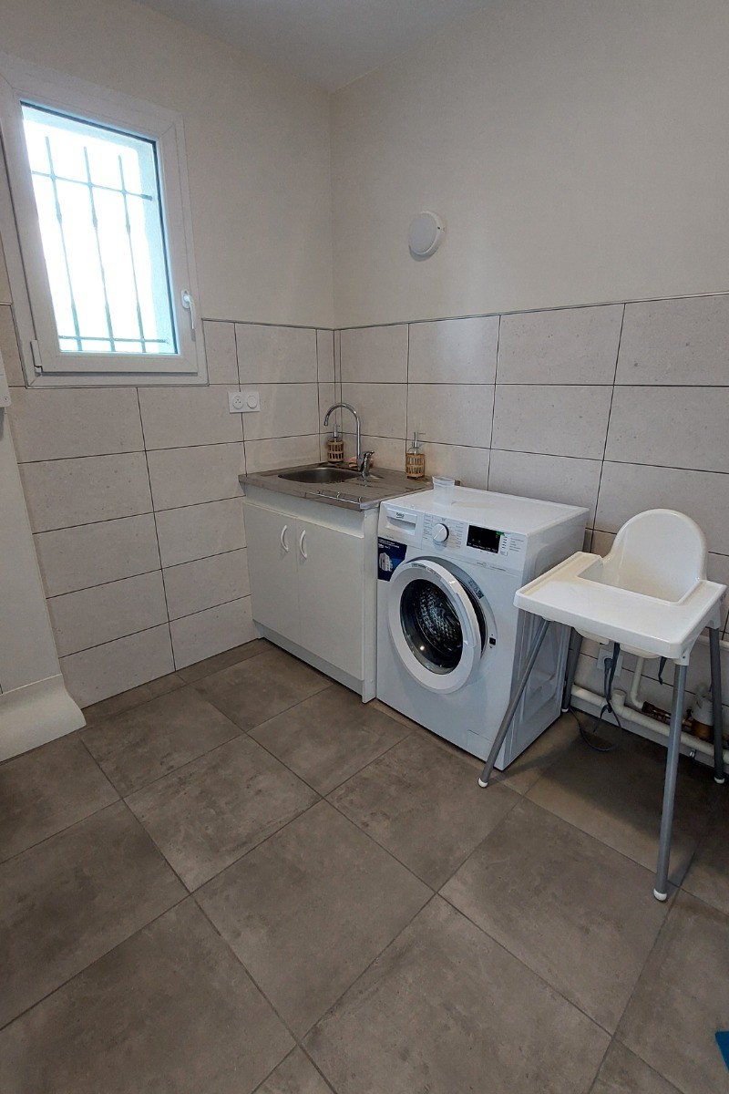 Buanderie du gîte La Petite Maison équipée d'une machine à laver, évier et rangements.