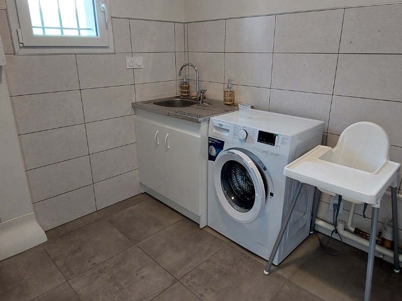 Buanderie du gîte La Petite Maison équipée d'une machine à laver, évier et rangements.