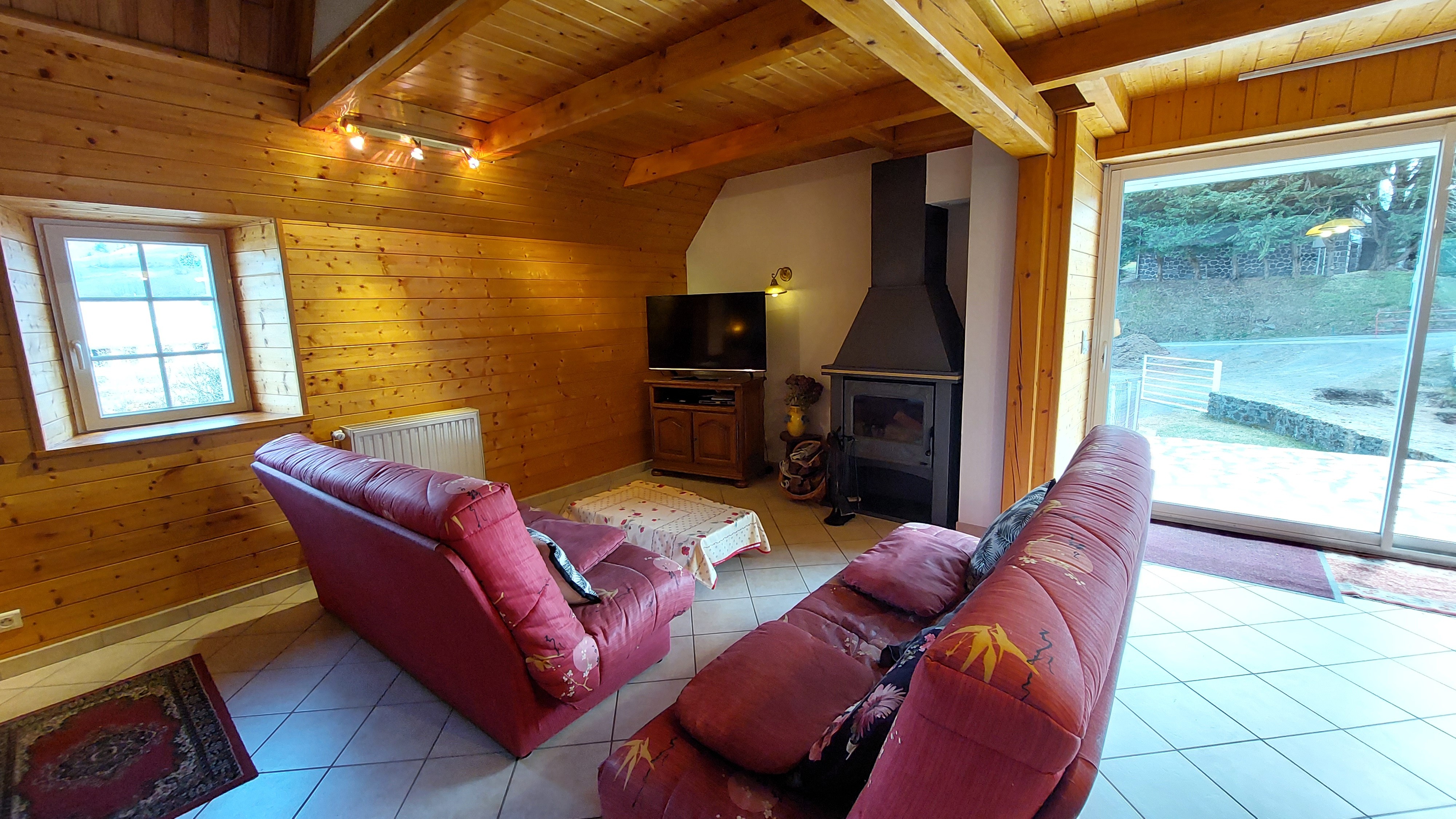 Cosy living room with sofa, wood-burning stove and access to terrace in gîte in Claux Cantal