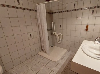Salle d'eau accessible aux fauteuils roulants dans une chambre d'hôtes PMR, avec douche et aménagement adapté.