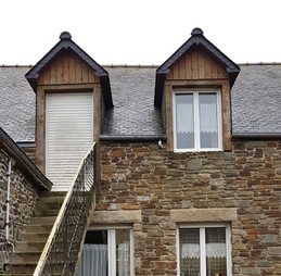 Façade de la maison de pays, en pierre de caractère. Stationnement privé devant la maison.