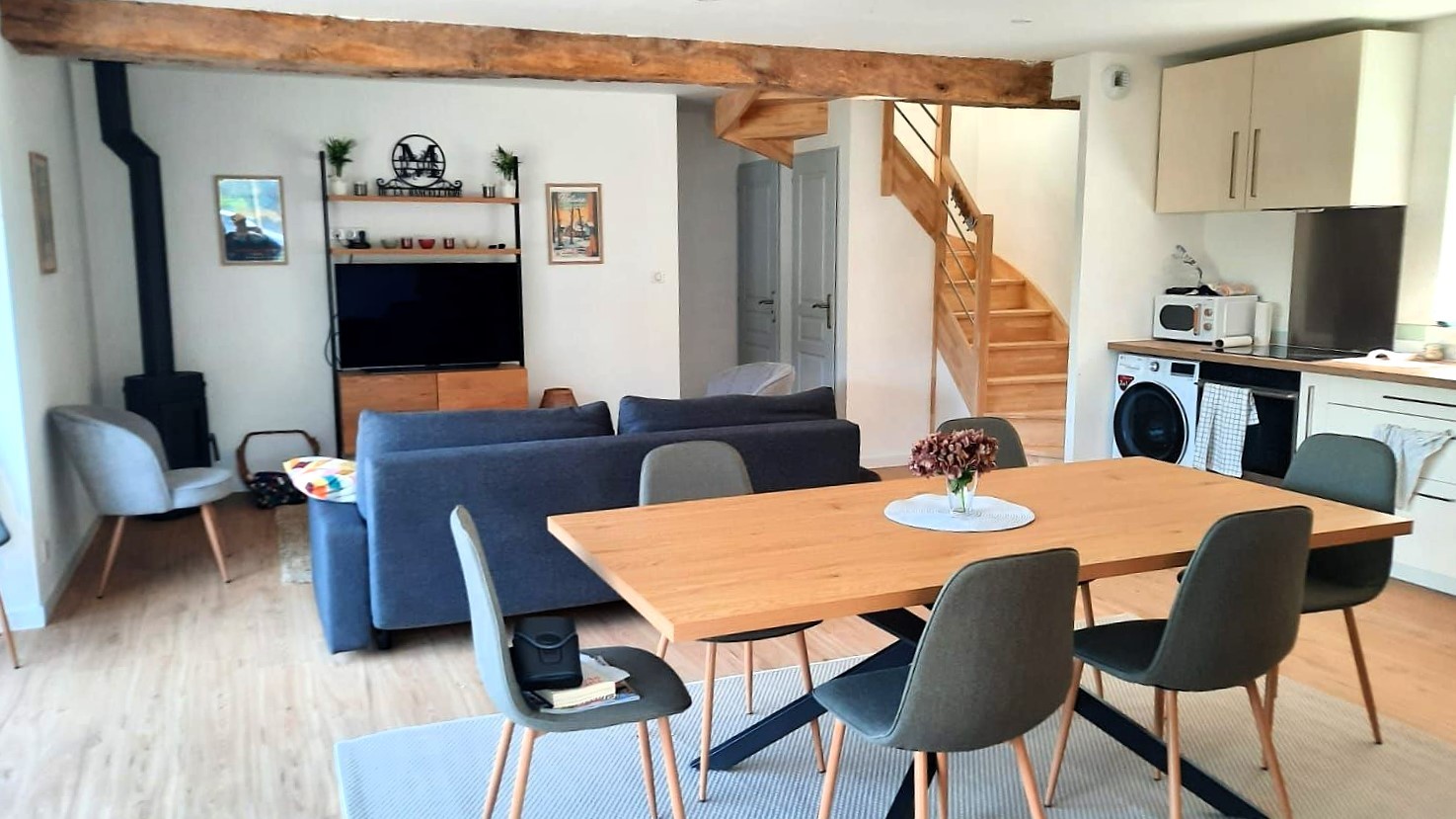 Grande pièce de vie avec salon (poêle à bois, smart TV), séjour et cuisine ouverte parfaitement équipée.