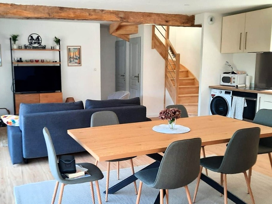 Grande pièce de vie avec salon (poêle à bois, smart TV), séjour et cuisine ouverte parfaitement équipée.