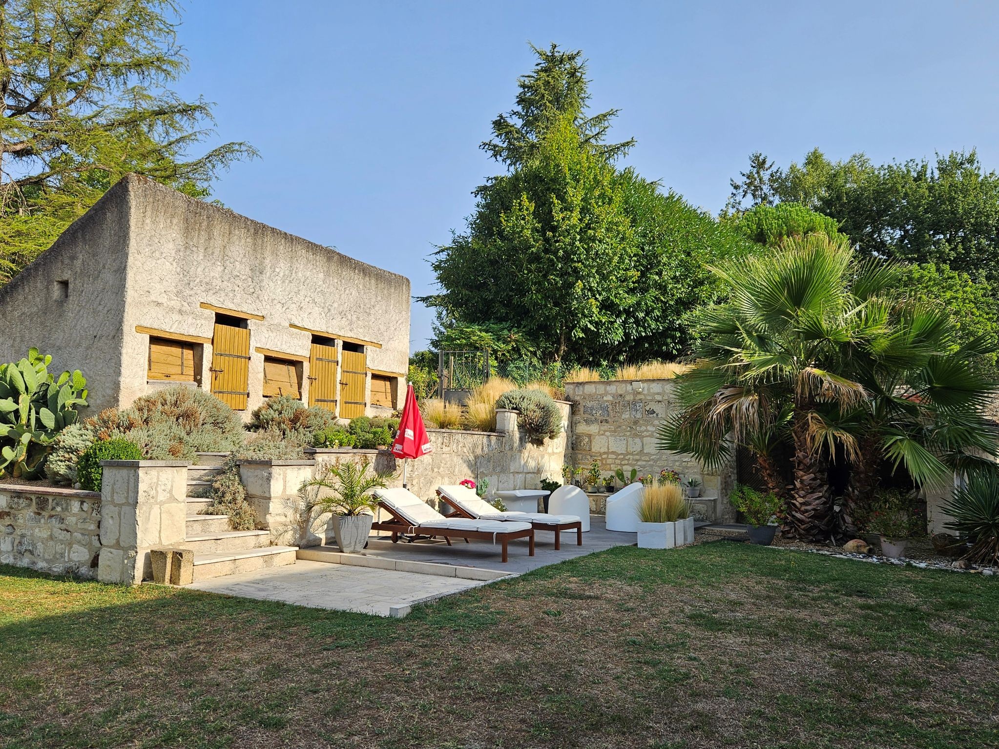 Terrasse extérieur avec transats, salon de jardin, parasols et coin abrité avec salon de jardin pour profiter des soirées