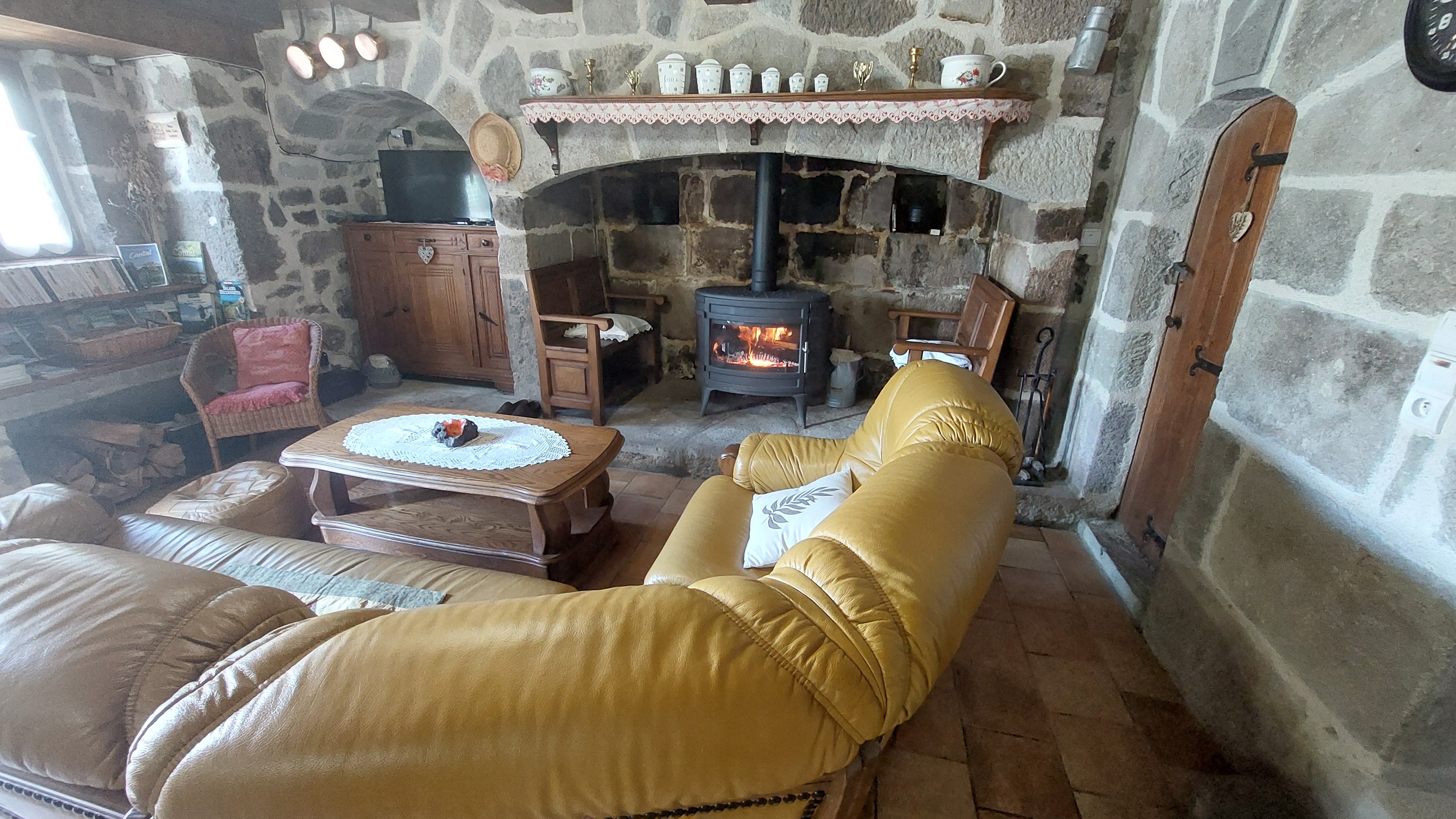 Cosy living room with stone fireplace and wood-burning stove in a Cantal gîte