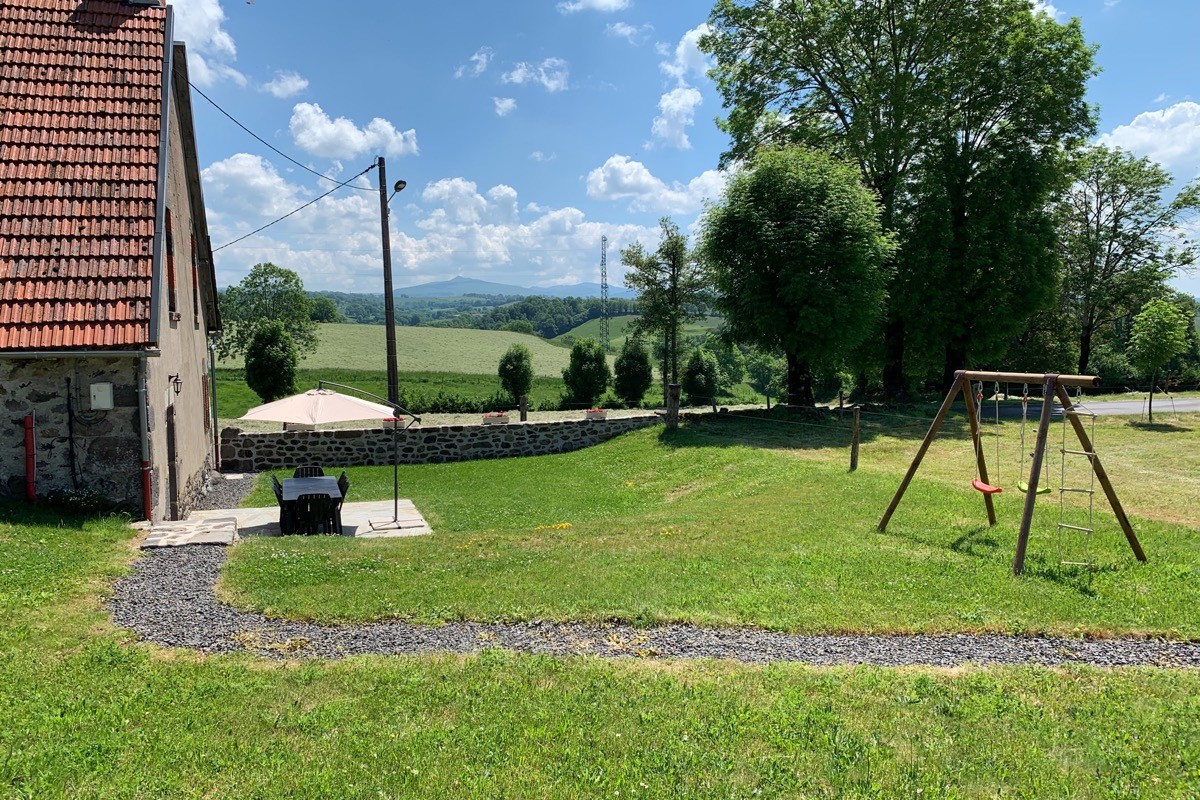 Le jardin avec une balançoire, une table de salon de jardin, le parasol et un barbecue.