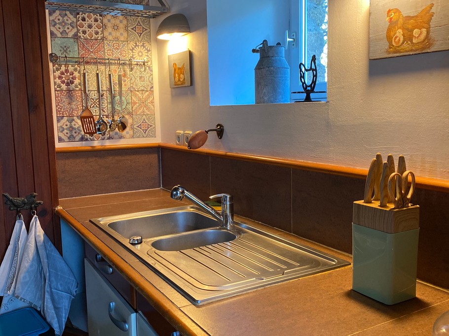 Grande pièce de vie au rez-de-chaussée avec espace cuisine toute aménagée et son mini bar, espace séjour, espace (vrai) bureau, et espace salon avec canapé en cuir, poêle à bois et TV.