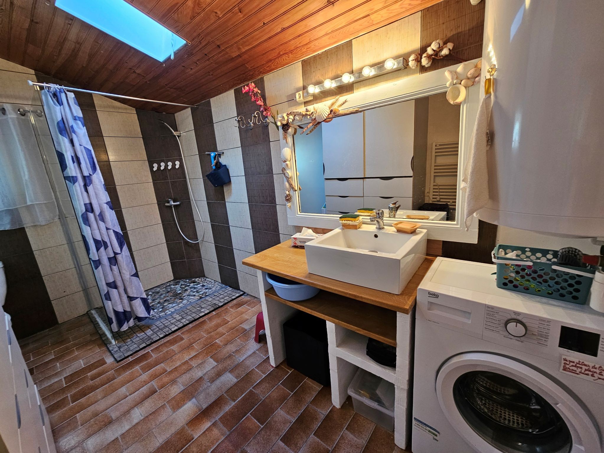 La grande salle d'eau avec douche à l'italienne, vasque sur meuble, WC, placards fermés et lave linge