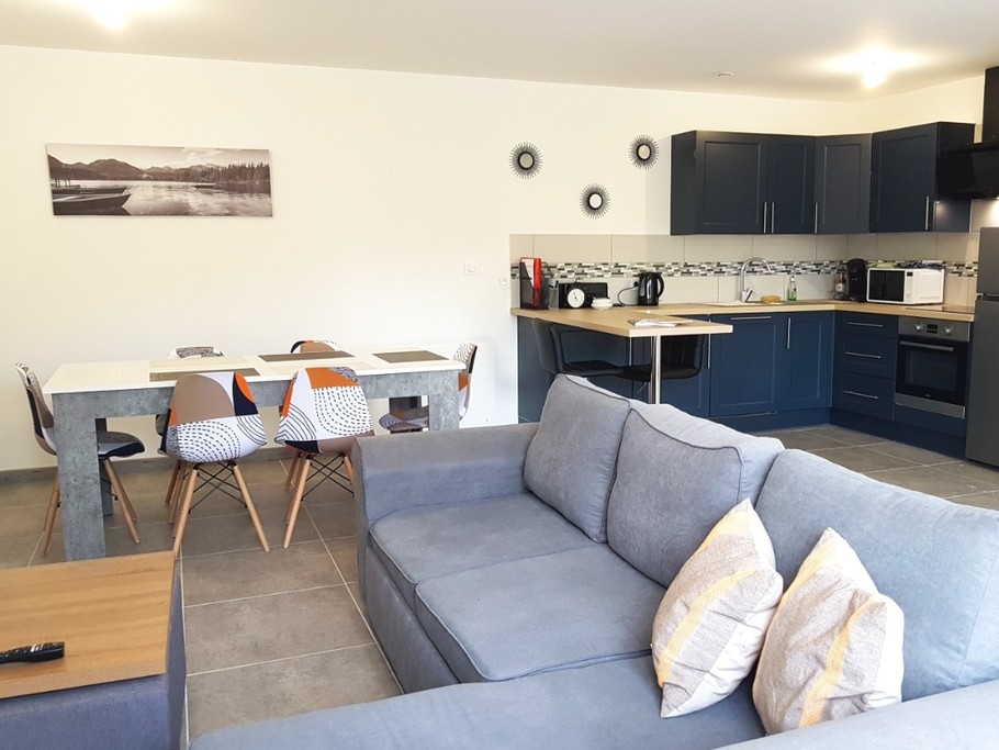 Grande pièce de vie de 32 m² avec coin cuisine toute équipée, coin séjour et coin salon. Accès à la terrasse de plain-pied.