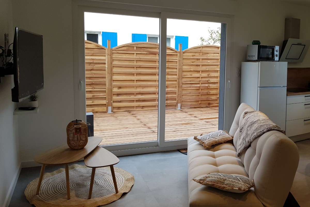 Pièce de vie au rez-de-chaussée avec coin salon avec TV, et coin cuisine et sa table à manger.  Canapé convertible pour 2 personnes. Terrasse en bois accessible par un portillon ou par la baie vitrée.
