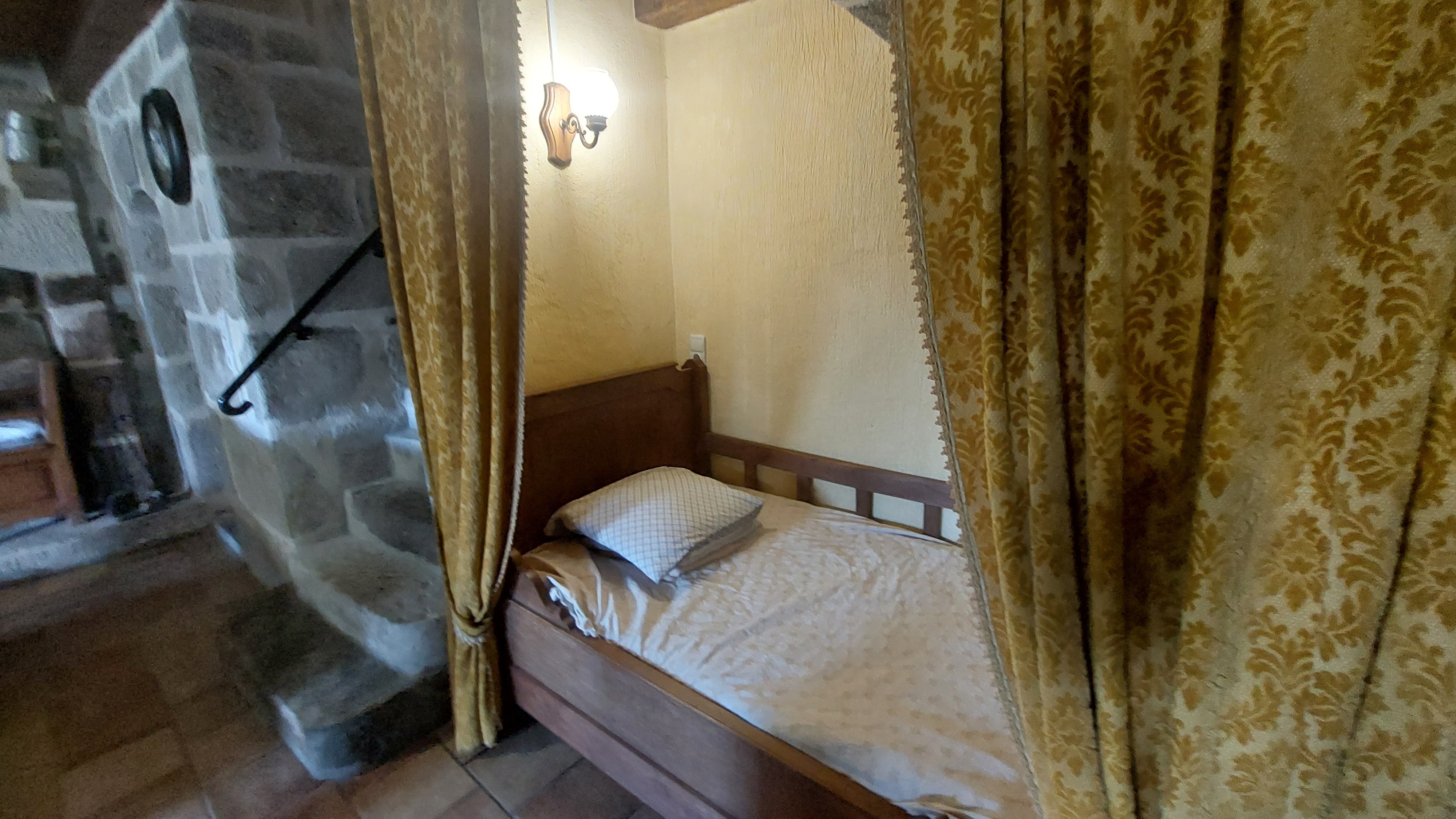 Single bed in alcove with curtains in rustic gîte in Cantal