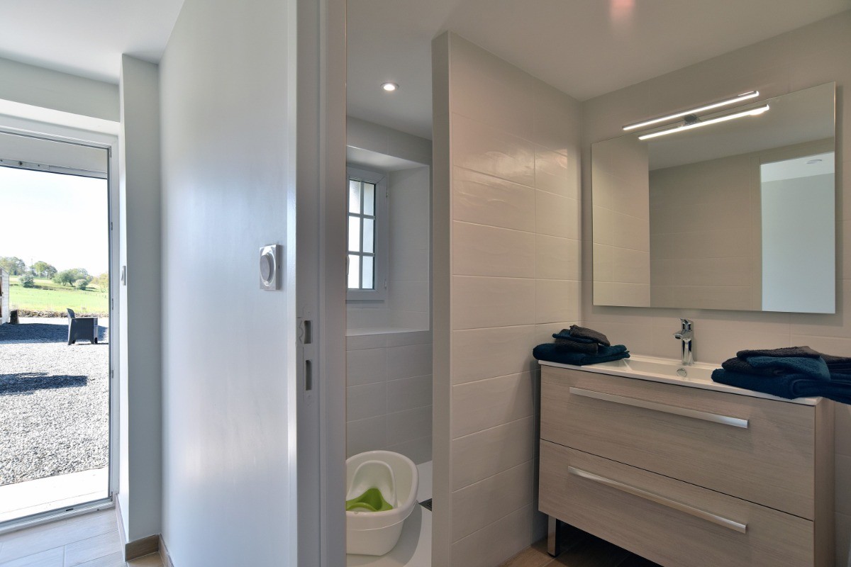 Salle d'eau avec douche à l'italienne spacieuse, meuble vasque et radiateur sèche serviette.