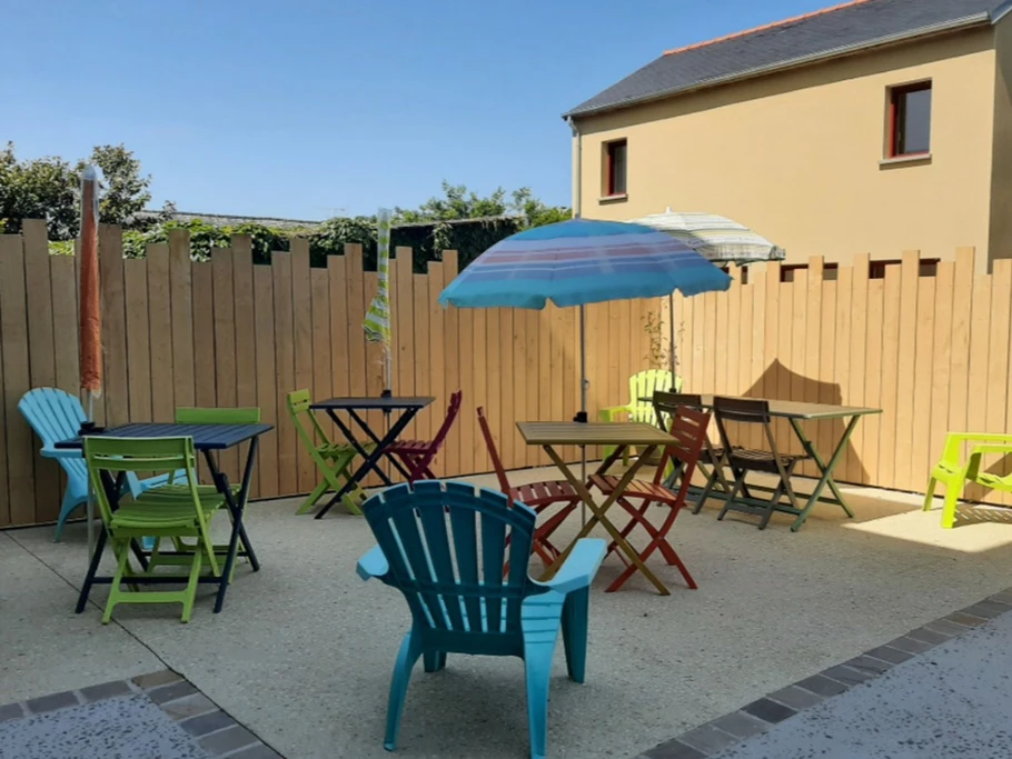 Terrasse ensoleillée au pied de la bâtisse, avec table de jardin, barbecue et abris pour vos équipements sportifs, à partager avec les autres vacanciers pour des moments conviviaux.