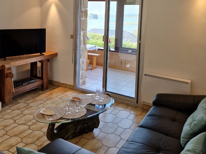 Salon vue mer donnant sur véranda panoramique et son coin repas, lecture et jeux