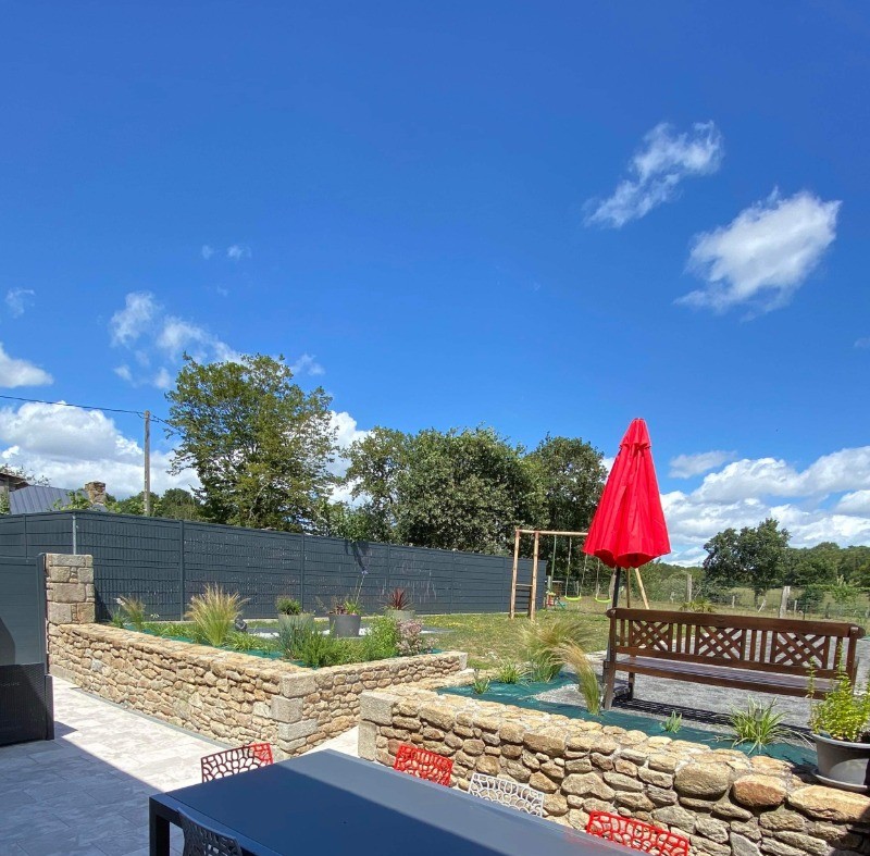 Terrasse avec table et salon de jardin. Dans le jardin, un boulodrome pour des parties de pétanque, un banc, une balançoire.