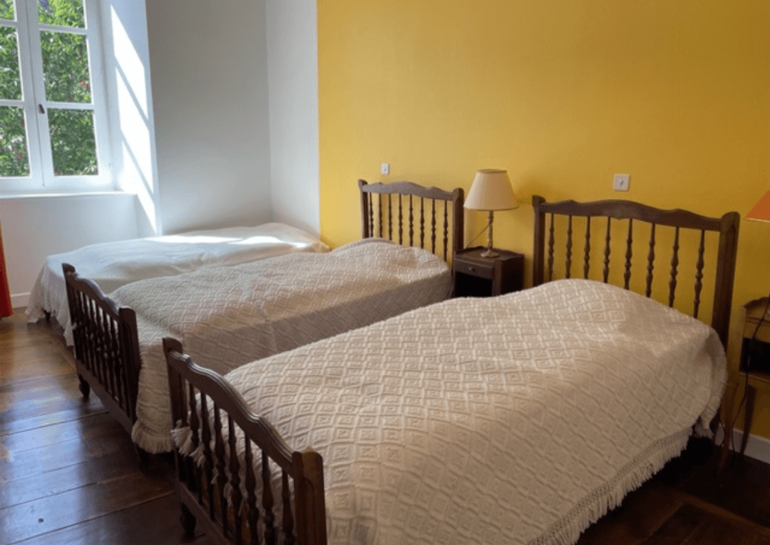 Chambre jaune chaleureuse avec trois lits simples, idéale pour les séjours en famille ou entre amis