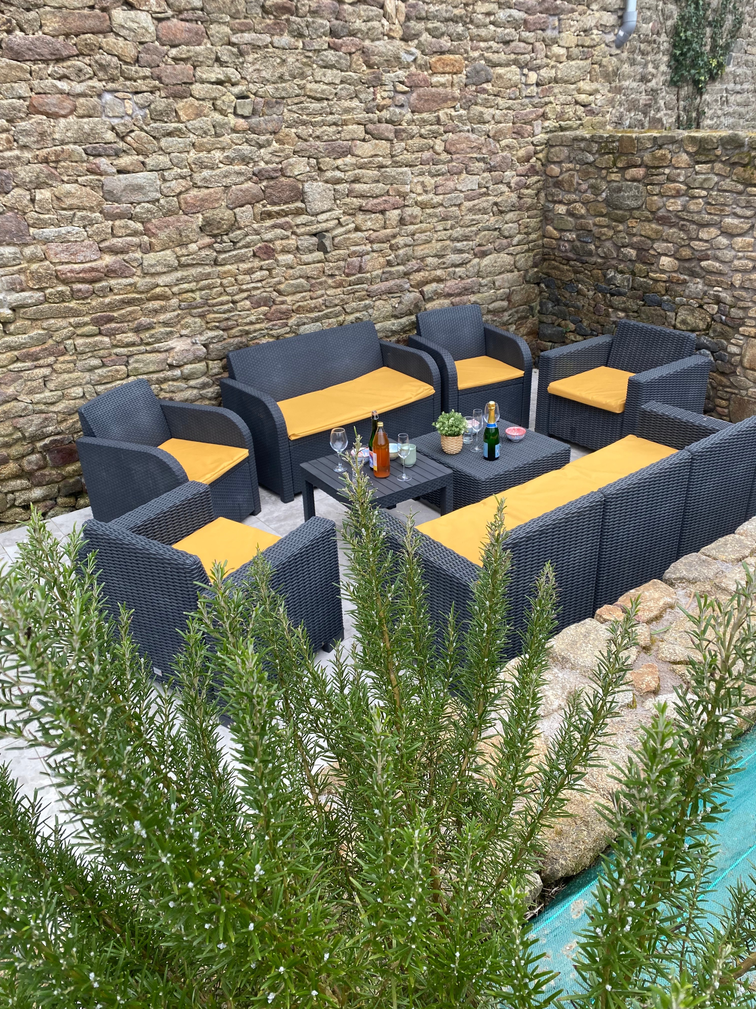 Terrasse avec table et salon de jardin. Dans le jardin, un boulodrome pour des parties de pétanque, un banc, une balançoire.