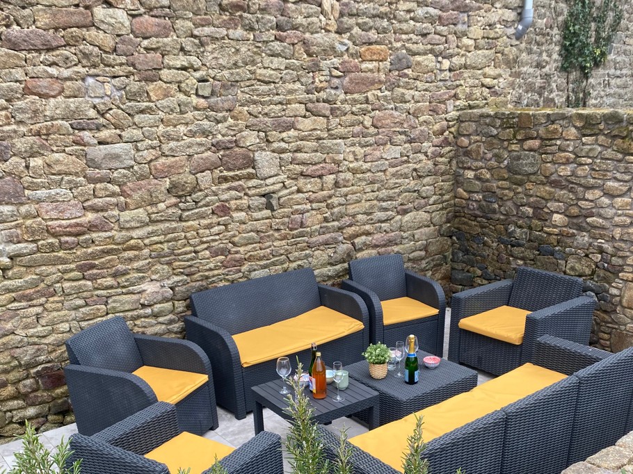Terrasse avec table et salon de jardin. Dans le jardin, un boulodrome pour des parties de pétanque, un banc, une balançoire.