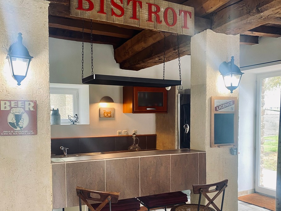 Grande pièce de vie au rez-de-chaussée avec espace cuisine toute aménagée et son mini bar, espace séjour, espace (vrai) bureau, et espace salon avec canapé en cuir, poêle à bois et TV.