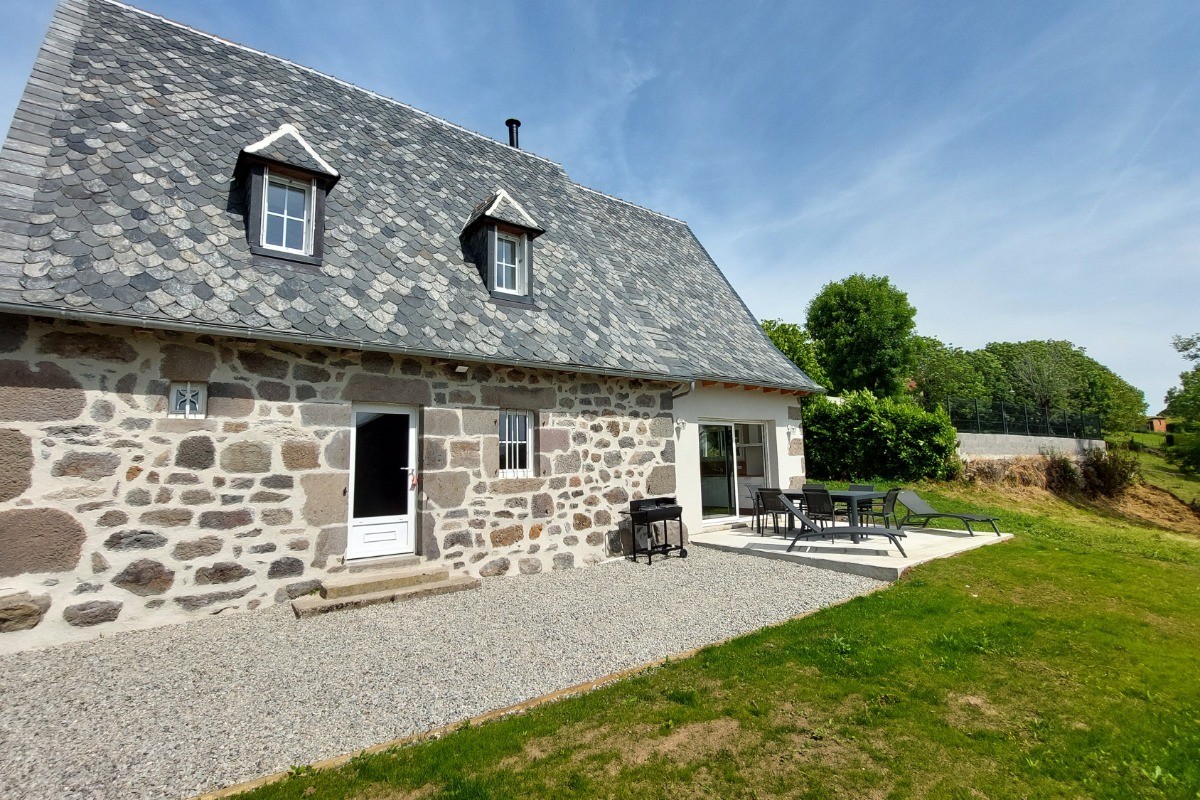 Terrasse extérieure du gîte La Petite Maison avec salon de jardin et transats, parfait pour se détendre sous le soleil du Cantal.