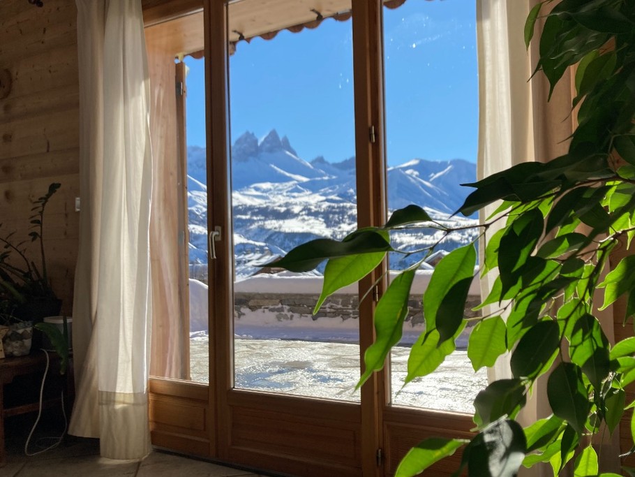 Salon avec télévision et poêle à bois, offrant une vue imprenable sur les montagnes et un accès direct à la terrasse.