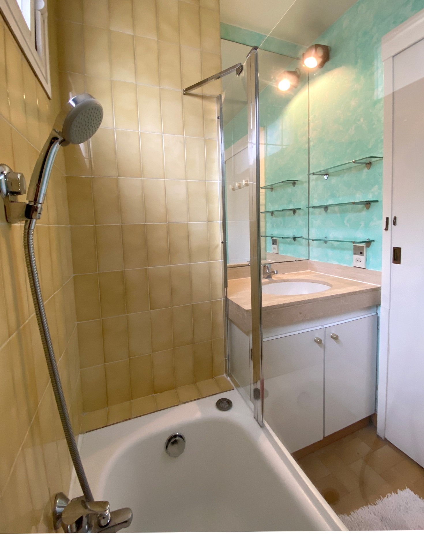 La salle de bains avec baignoire et son pare-douche, et un meuble-lavabo avec dessus en marbre.